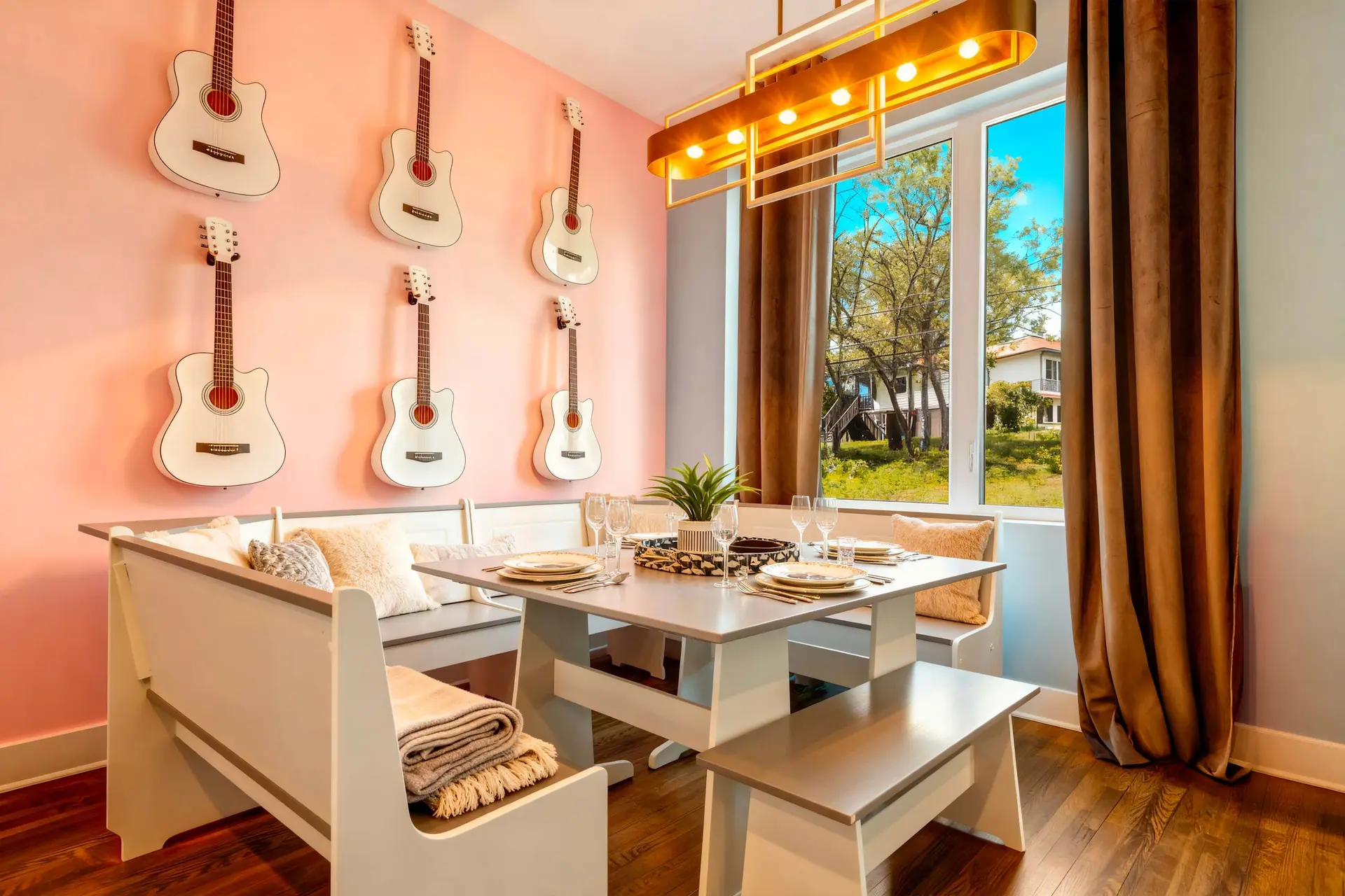 White guitars are mounted on a pink wall above a dining table with a bench and chairs.