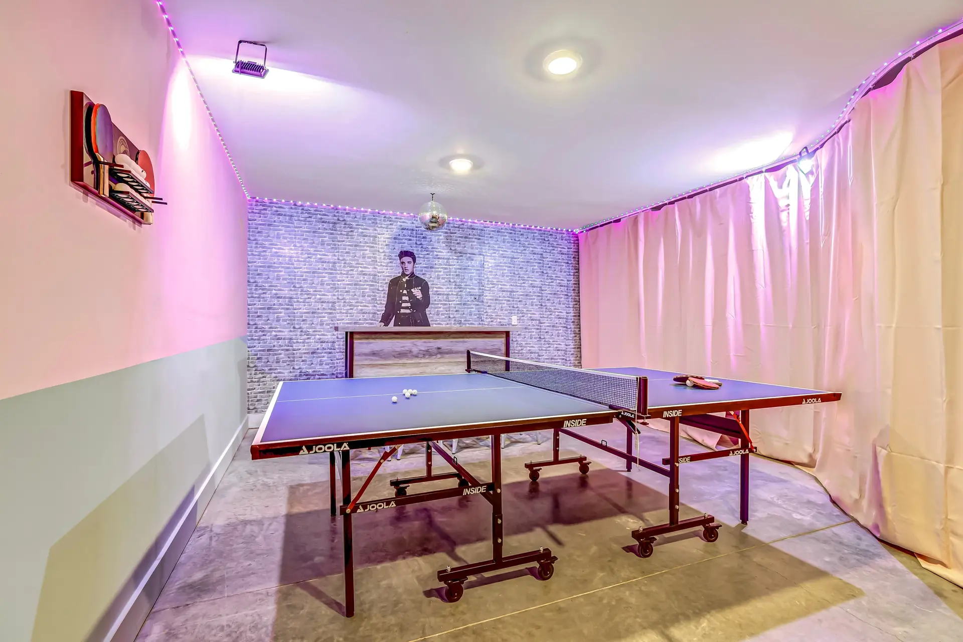 A ping pong table with balls and paddles sits in a room with colorful lighting.