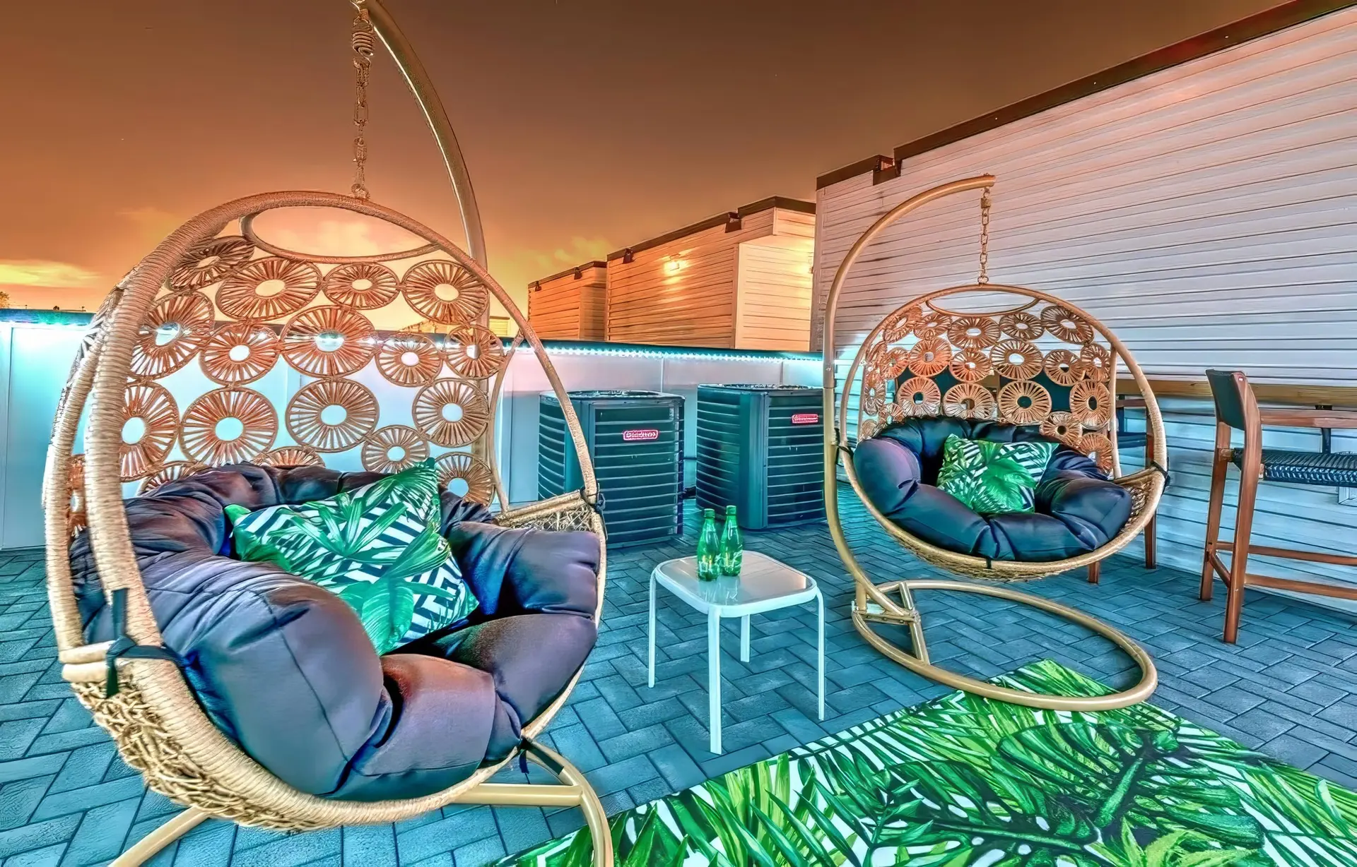 Two wicker hanging chairs with plush cushions sit on a patio.