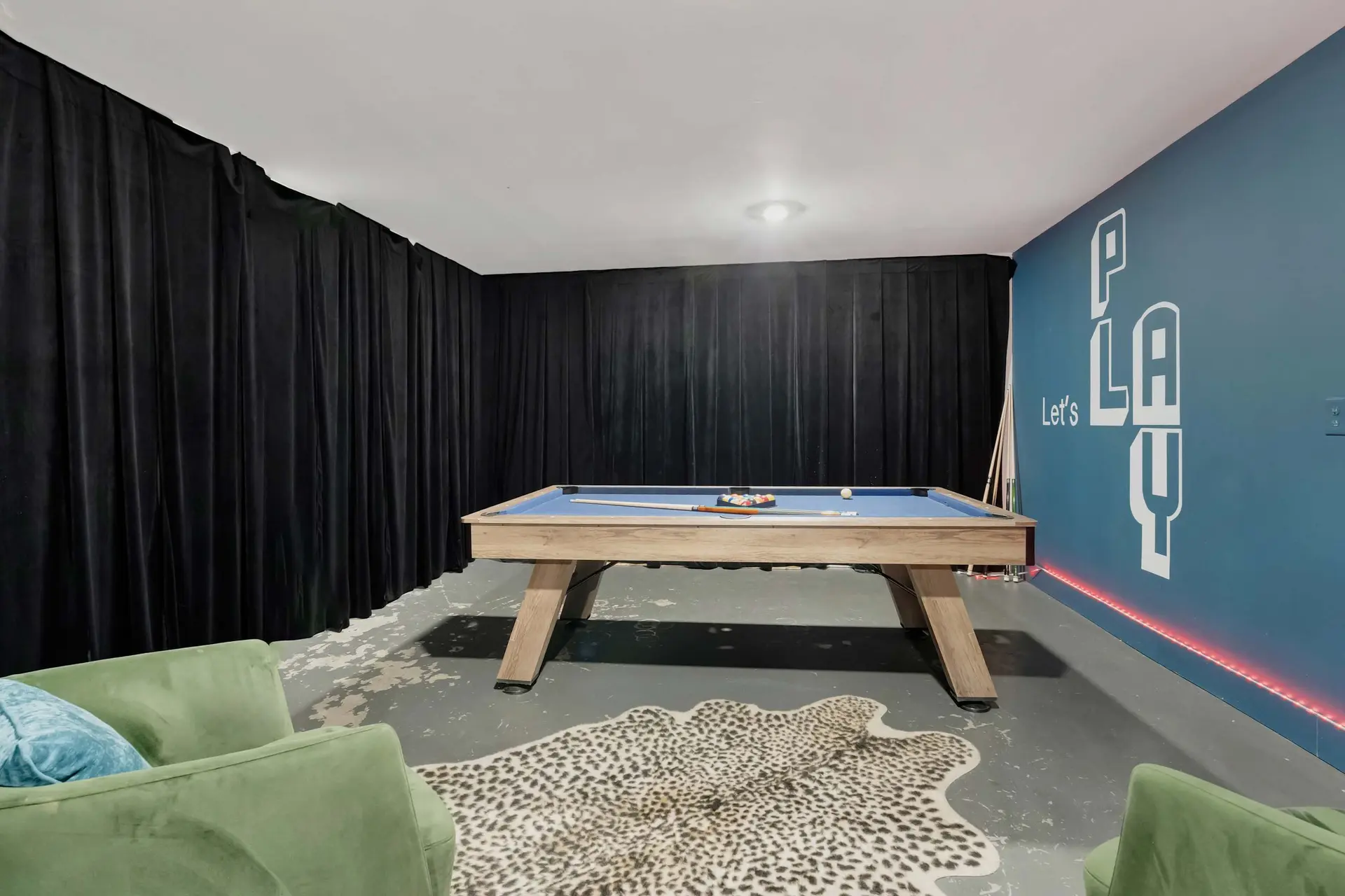 Pool table in a room with blue wall and black curtains.