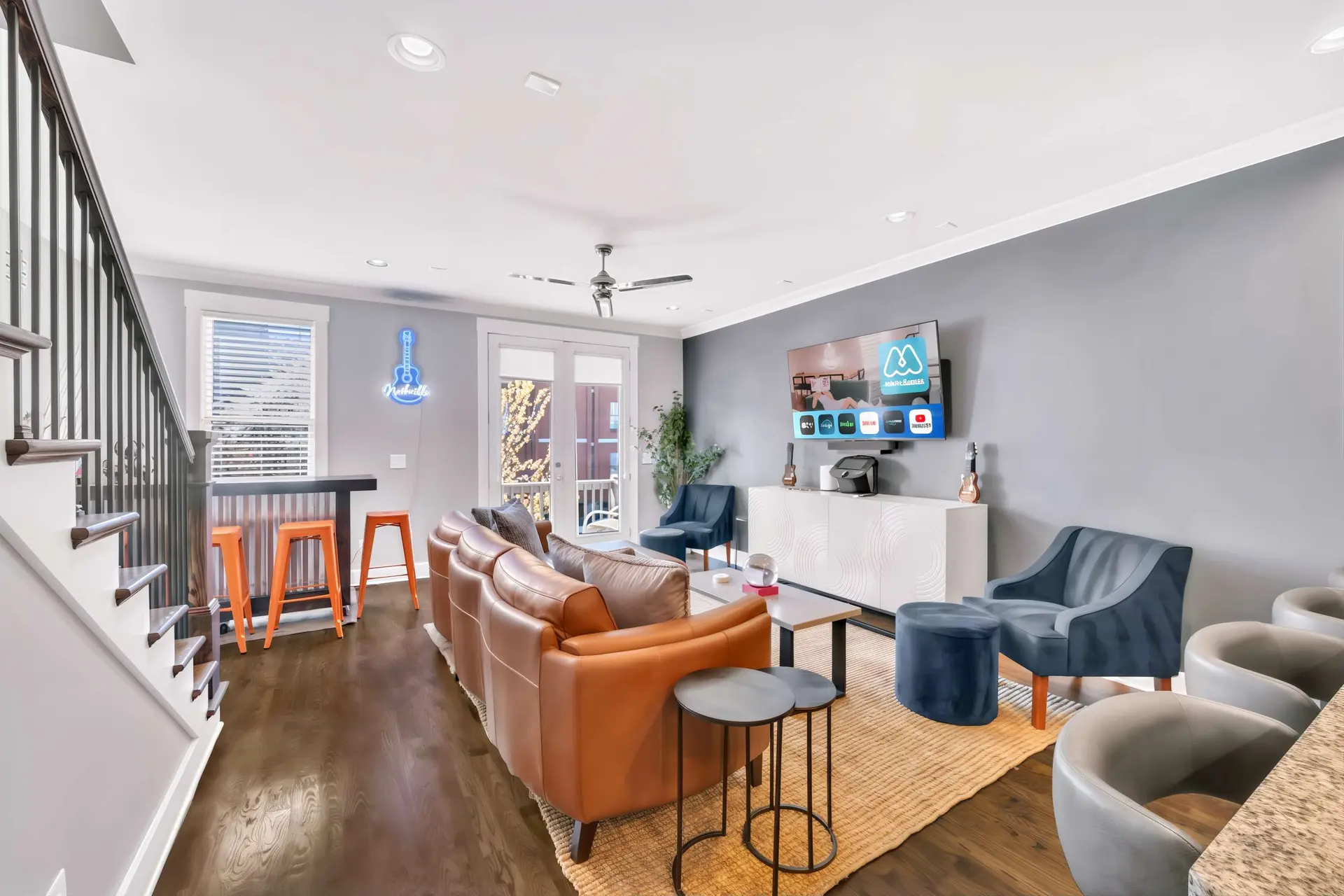 A living room with a tan leather couch, blue accent chairs, and a large TV.
