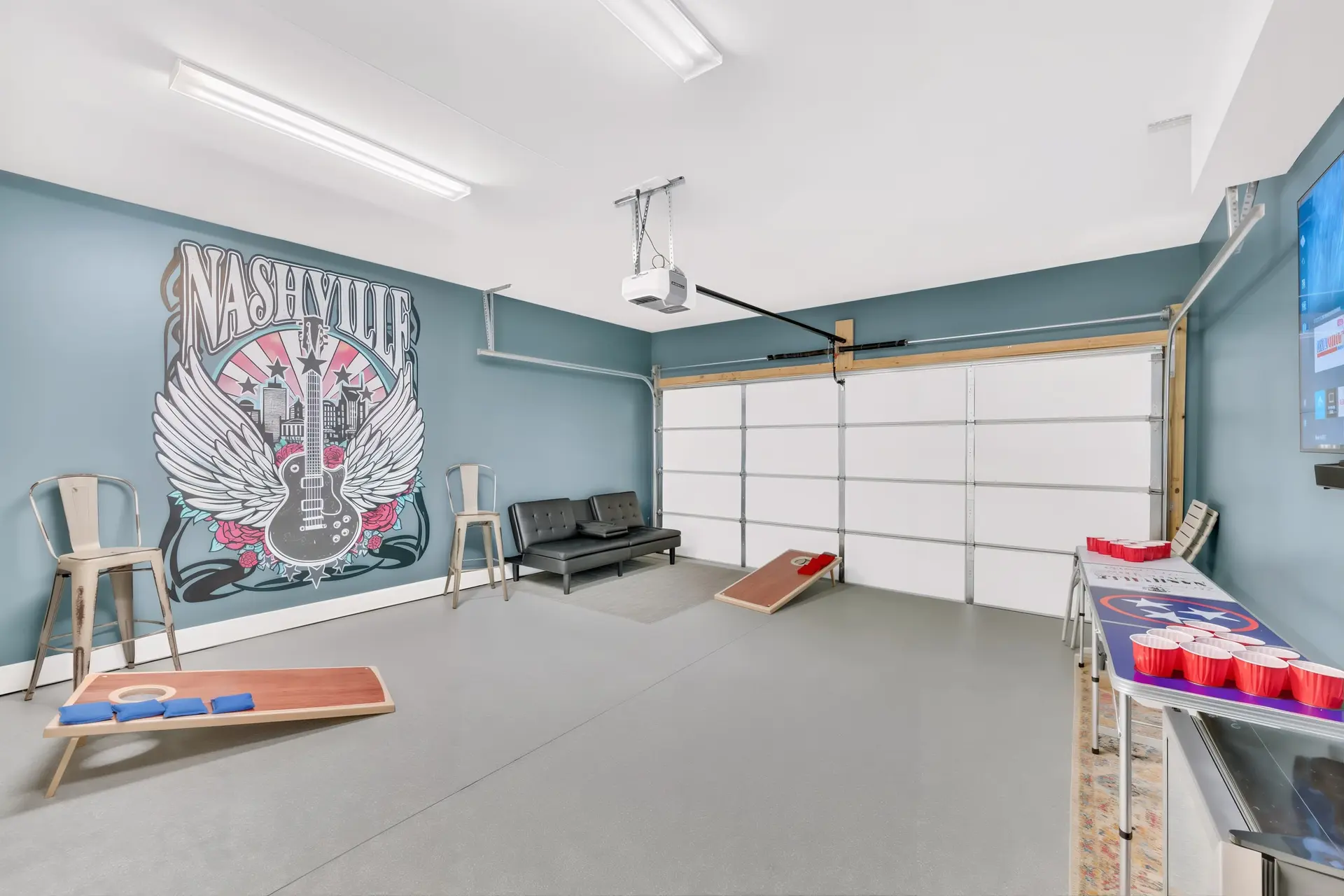 A garage with a Nashville mural, a couch, and two cornhole boards.