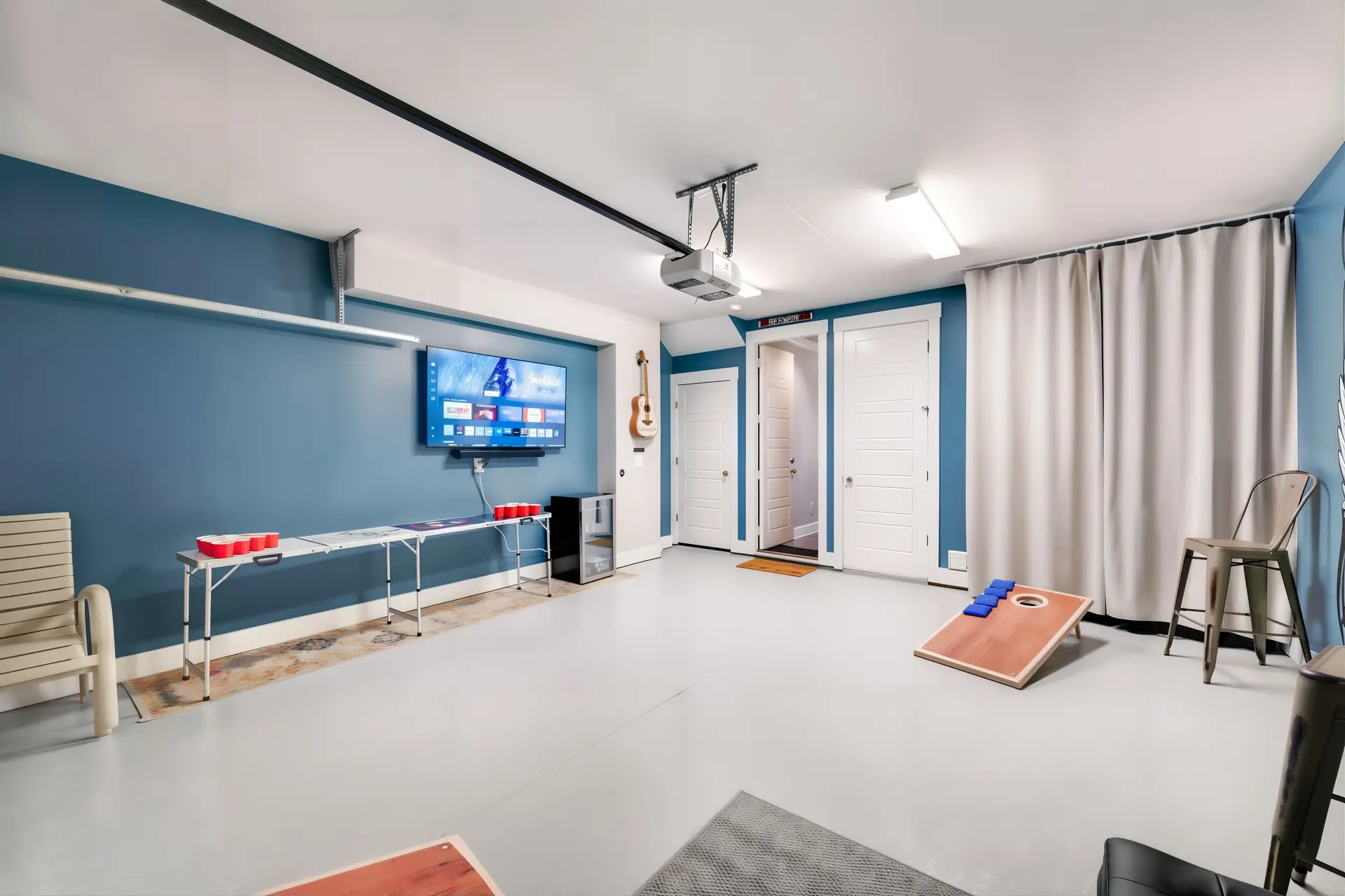 An indoor garage game room with a TV, projector, beer pong table, and cornhole set.