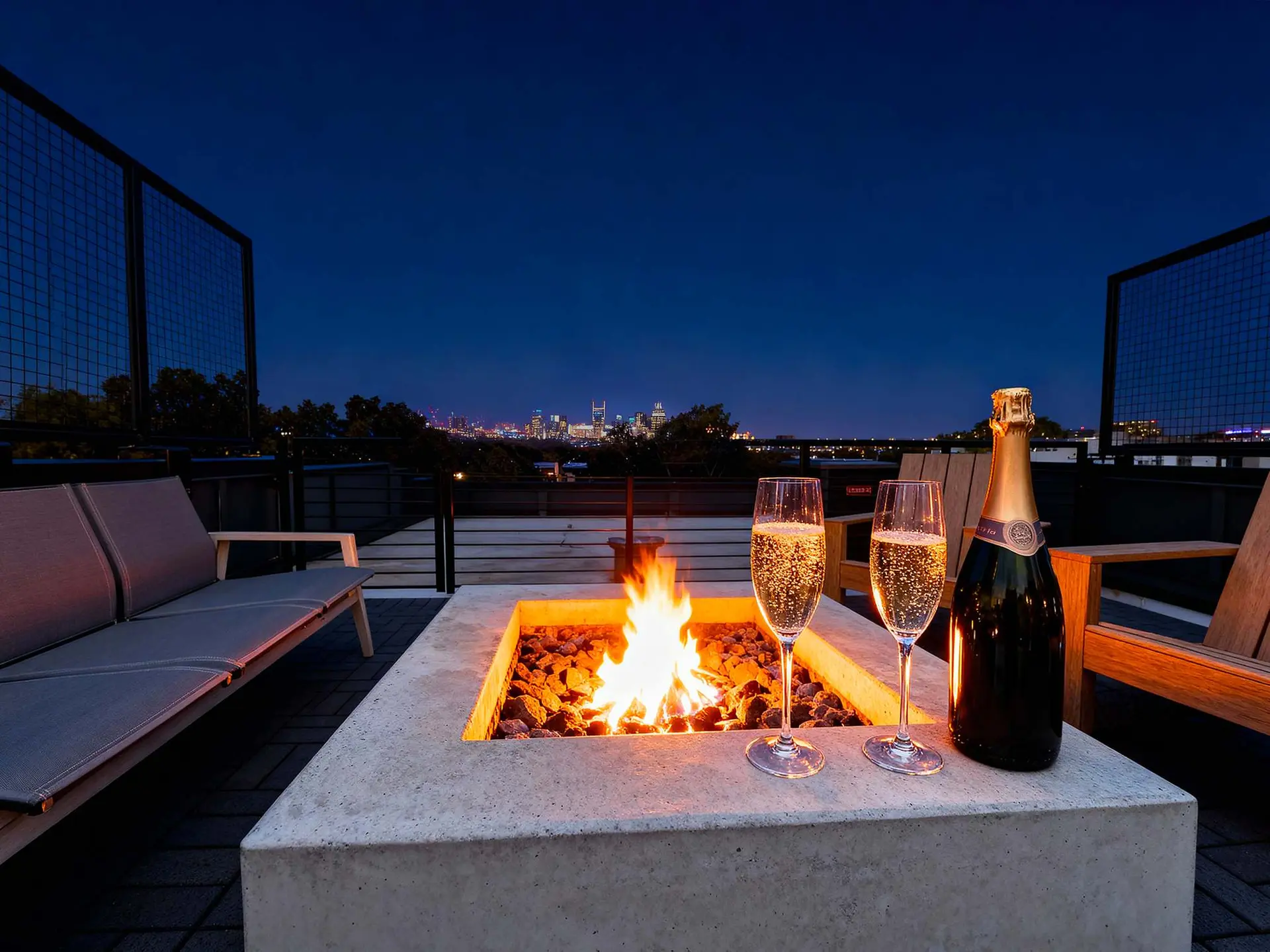 A rooftop fire pit at night with city lights, champagne, and glasses.