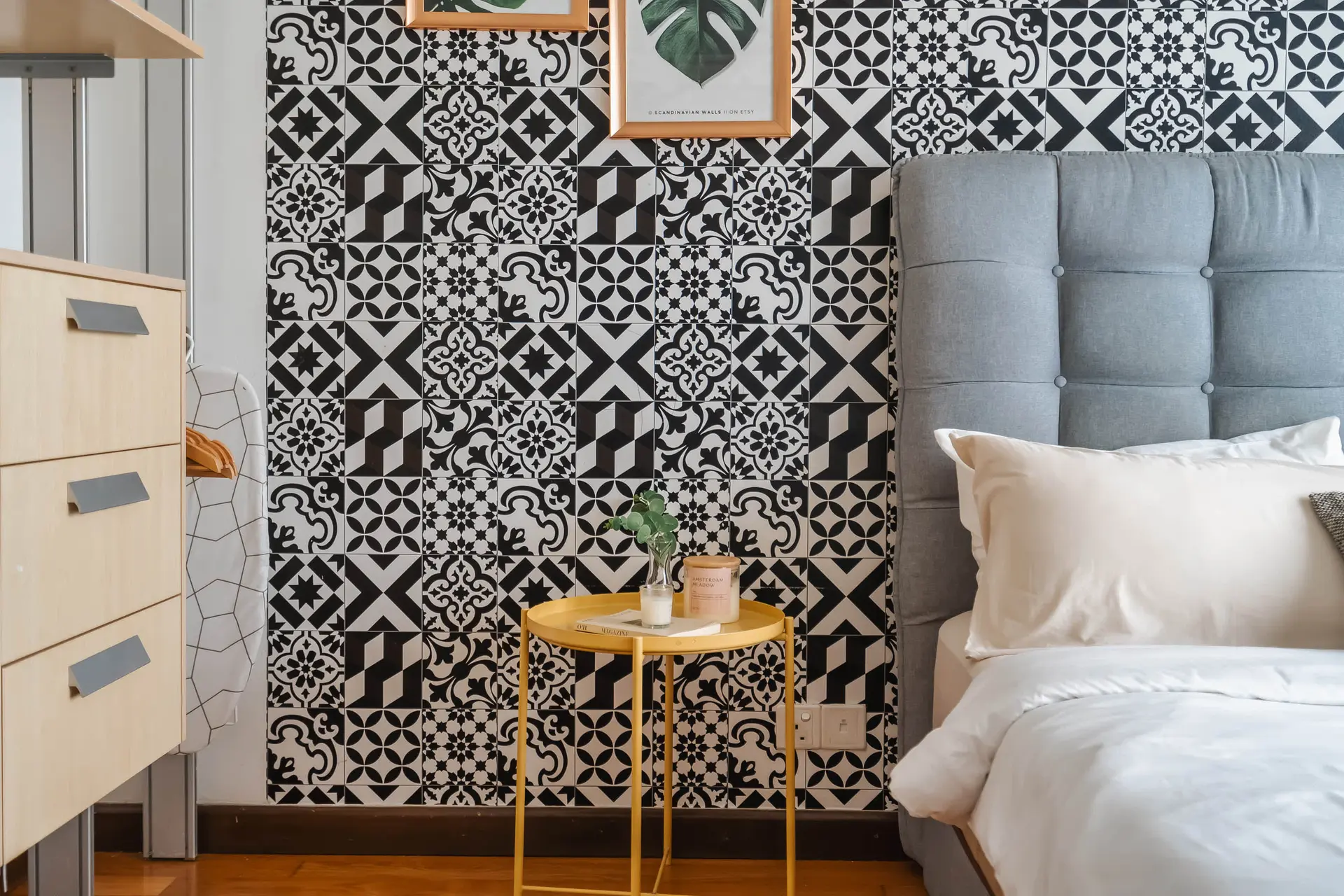 A bedroom with a patterned tile wall, a gray headboard, and a wooden nightstand.