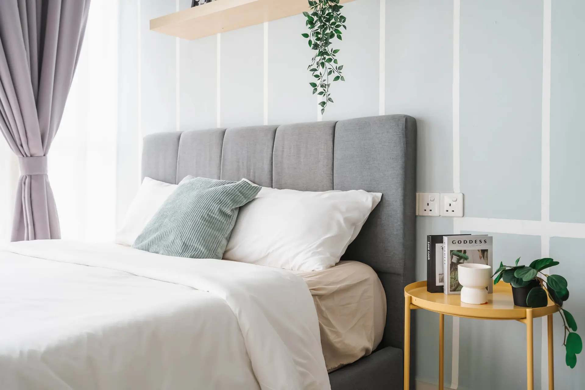 A bed with gray upholstered headboard, white linens and pillows, and a green throw pillow.