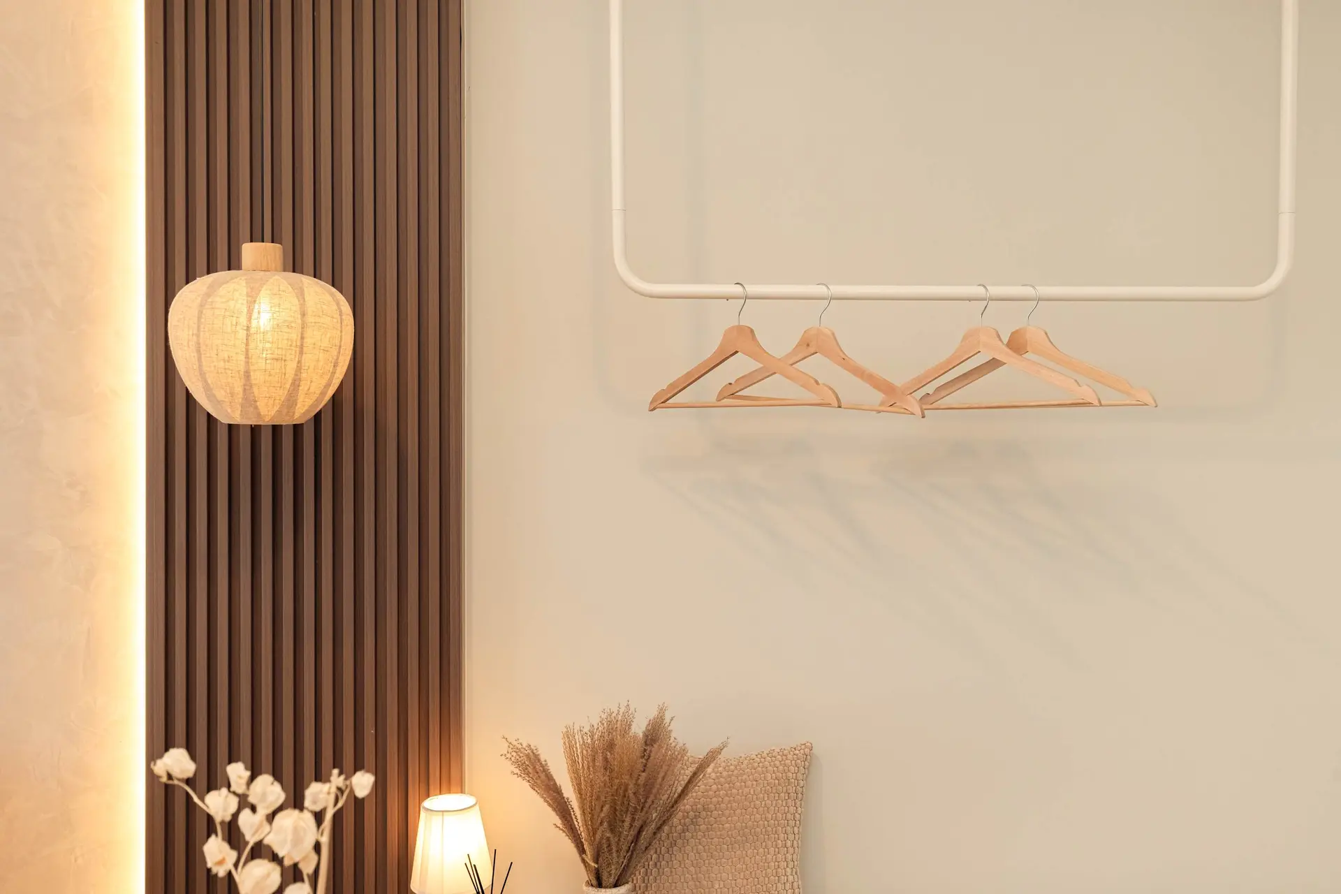 A cream-colored wall with a clothing rack and hangers hangs above a beaded pillow and dried flowers.