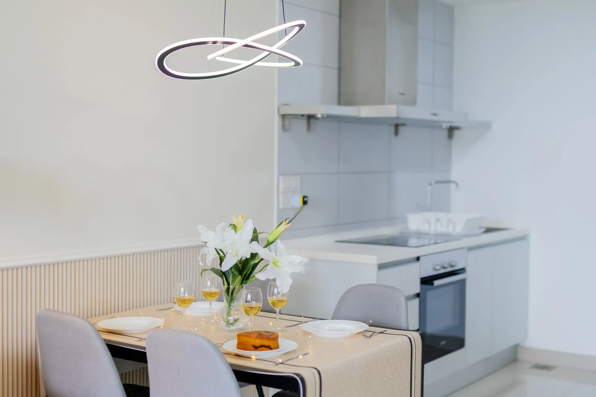 A modern dining room with a table set for four people with glasses of wine and a cake.