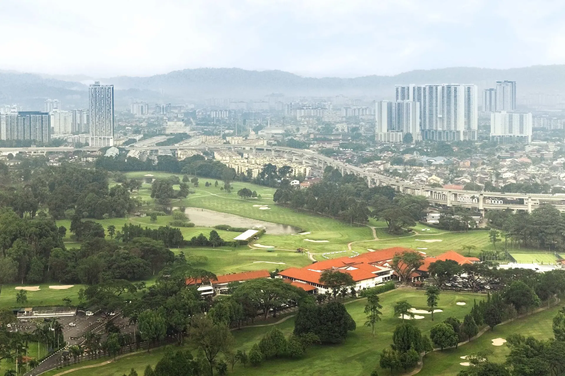 Aerial view of a city with skyscrapers, a highway, a golf course, and a building with a red roof.