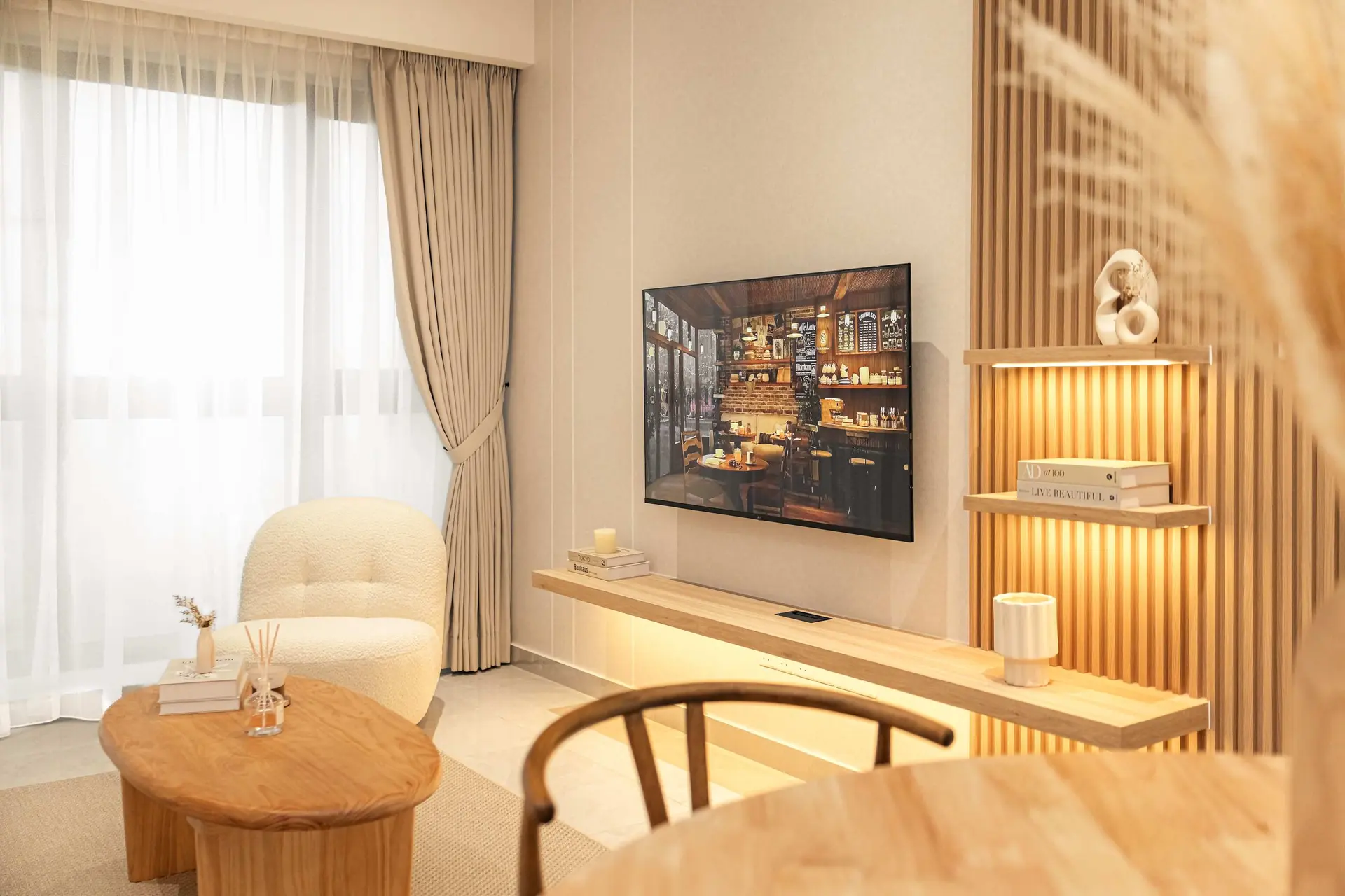 A modern living room with a TV, shelving, and soft, neutral furniture.