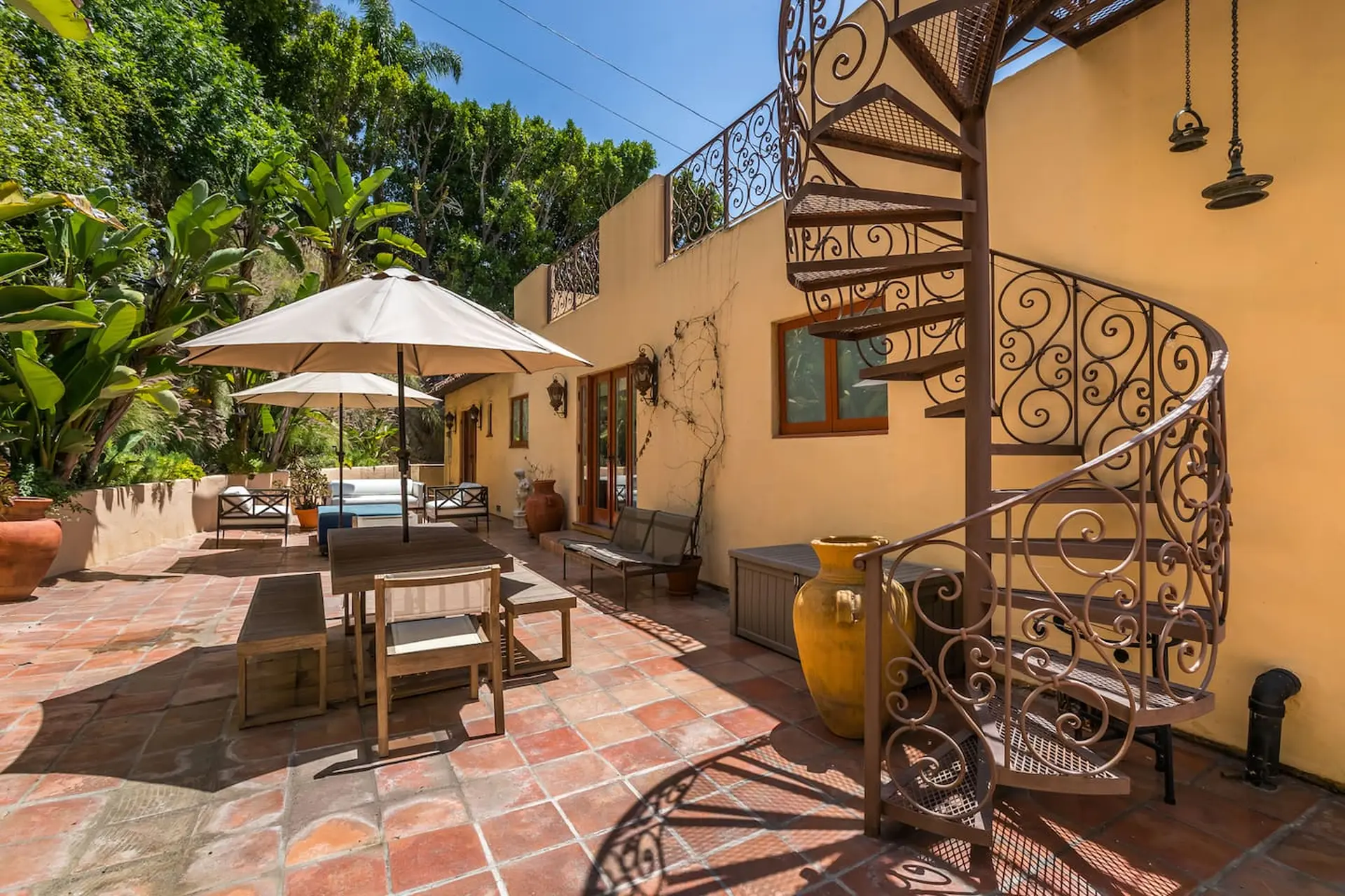 Terracotta patio with outdoor dining, umbrellas, and spiral staircase.