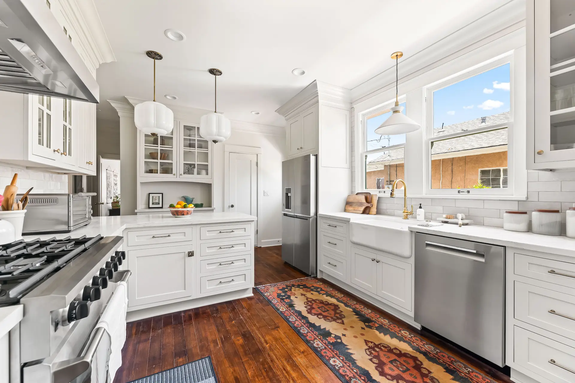A bright, white kitchen with stainless steel appliances and a colorful rug.