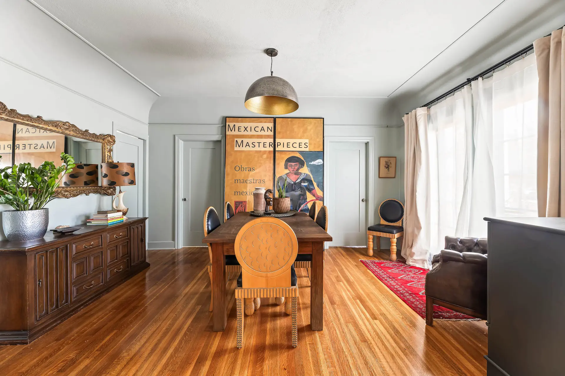 A dimly lit dining room with a wood table and chairs, a dresser, and art on the walls.