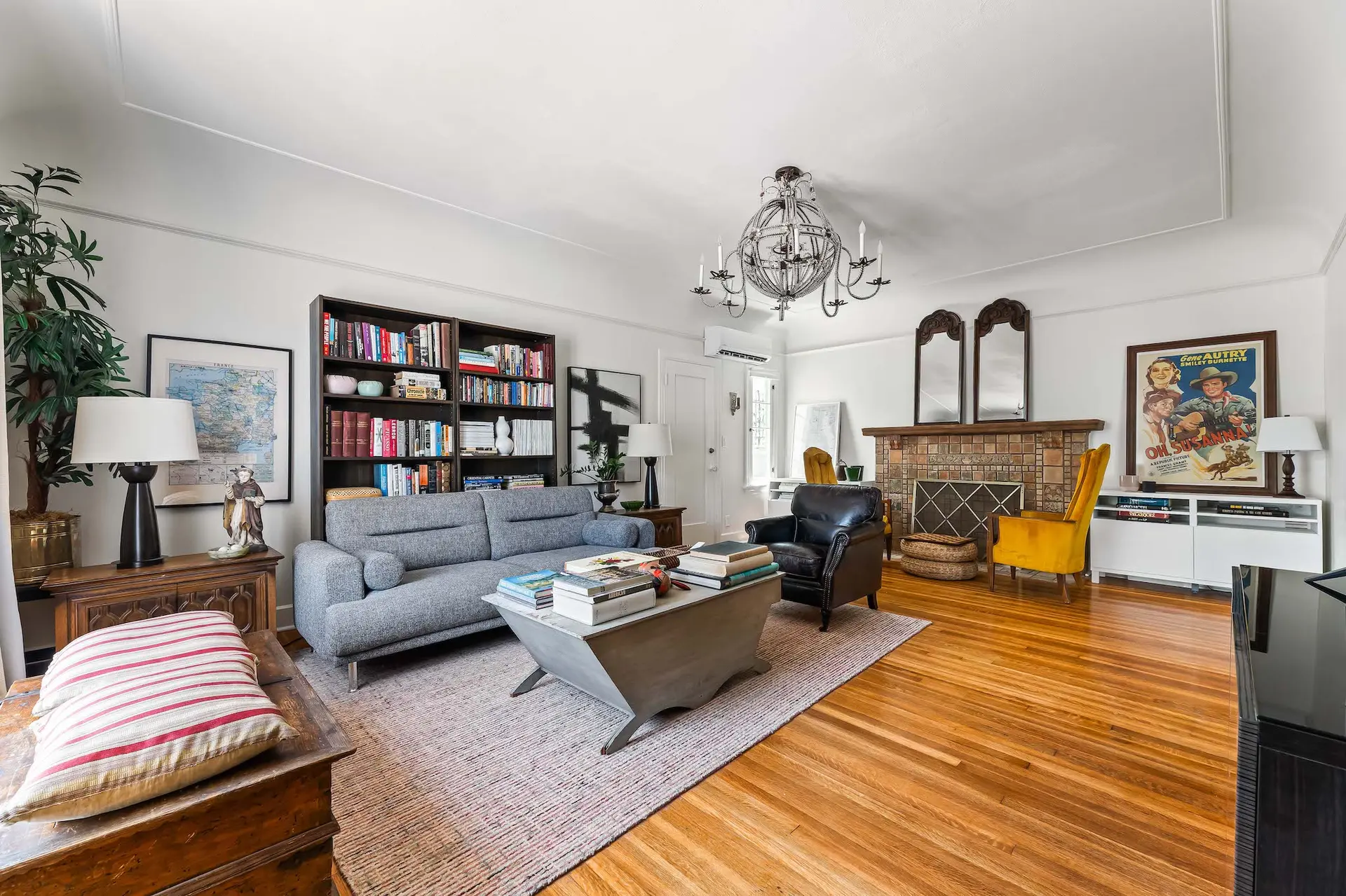 A living room with a gray sofa, armchair, fireplace, and bookshelf.