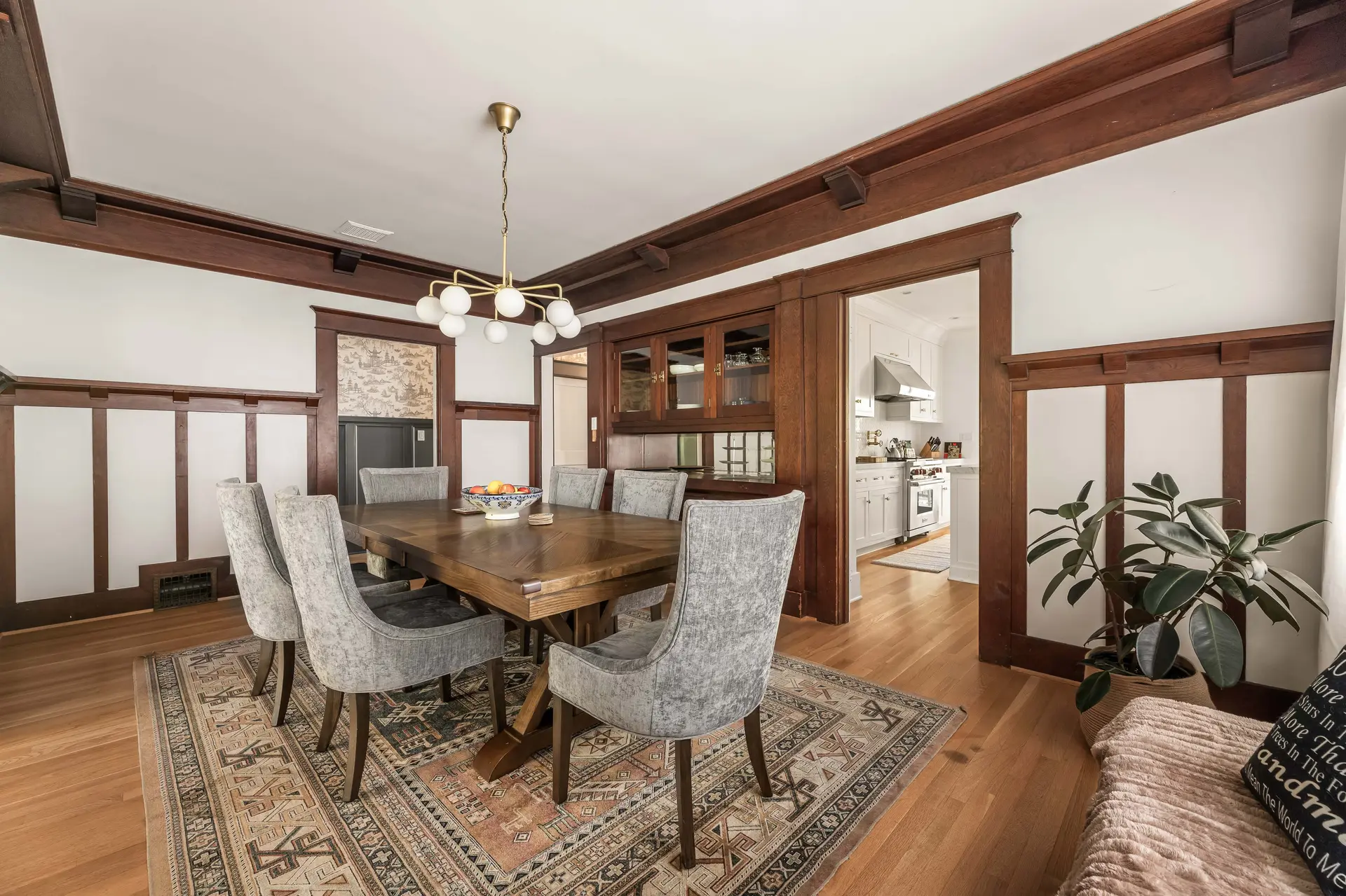 A dining room featuring a wooden table and chairs, a rug, and a kitchen view.