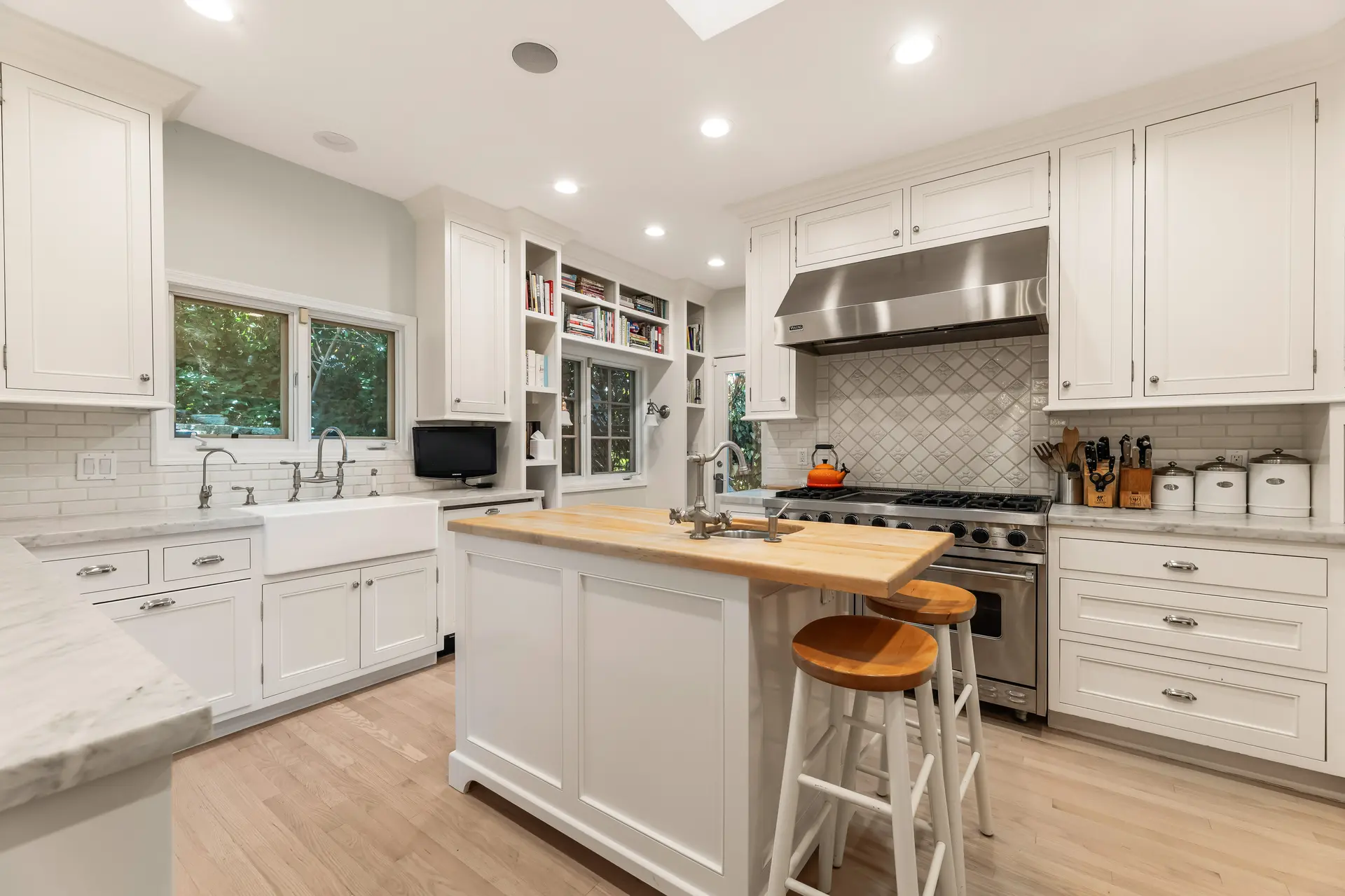 A bright, modern kitchen with white cabinets, a butcher block island, and stainless steel appliances