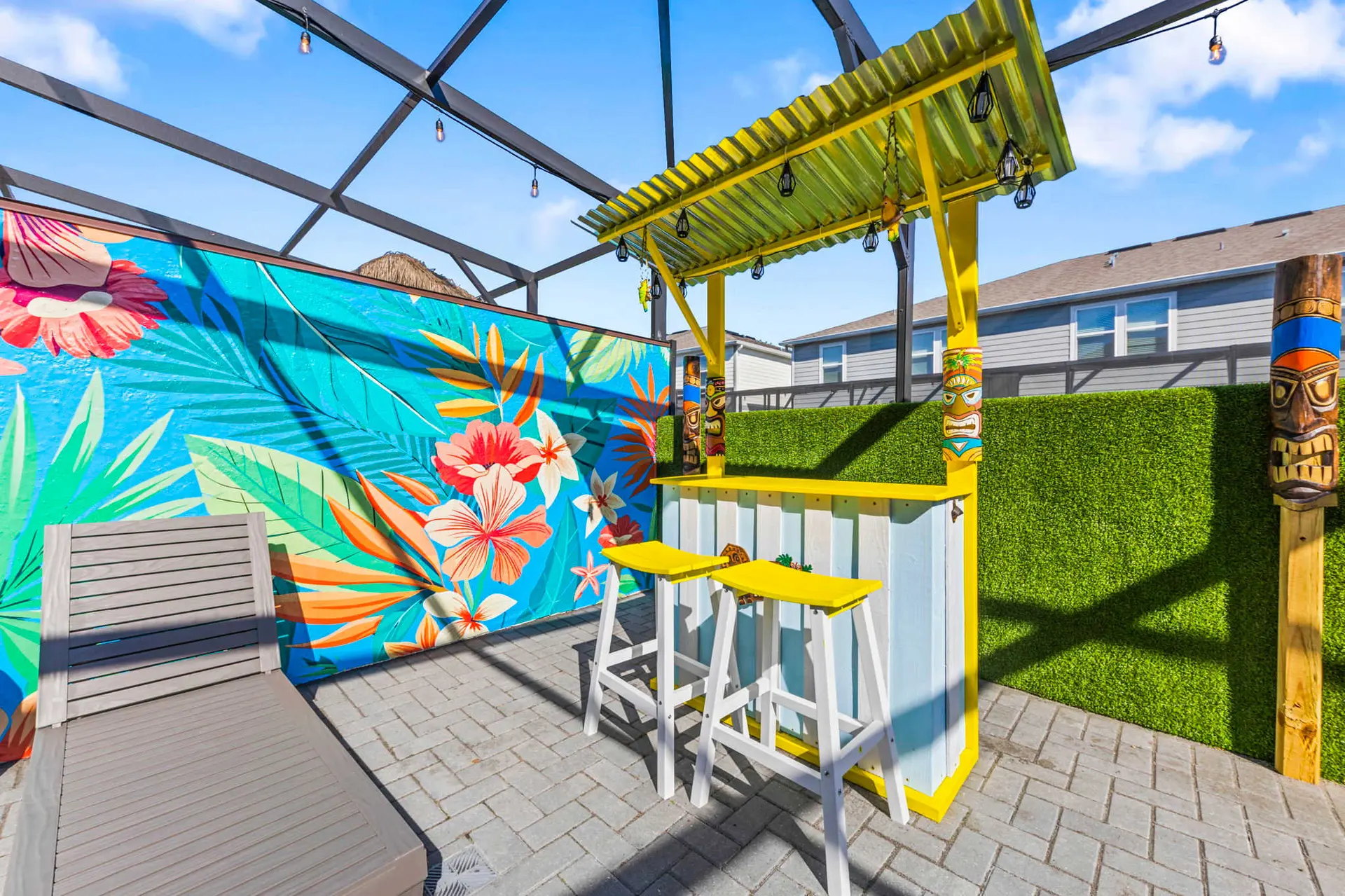 Outdoor tiki bar with colorful mural, bar stools, and tropical decor.
