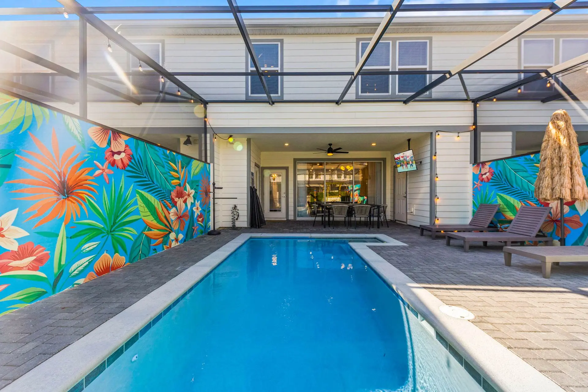 Tropical mural wall beside pool and lounge chairs under a covered patio.