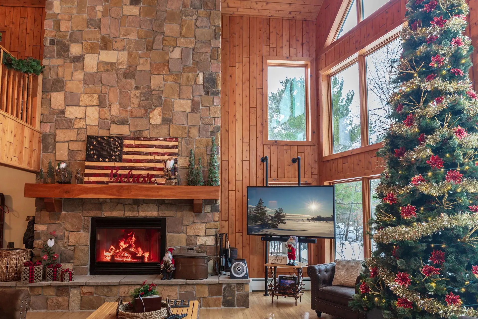 Cozy cabin living room decorated for Christmas with a stone fireplace, Christmas tree, and large win