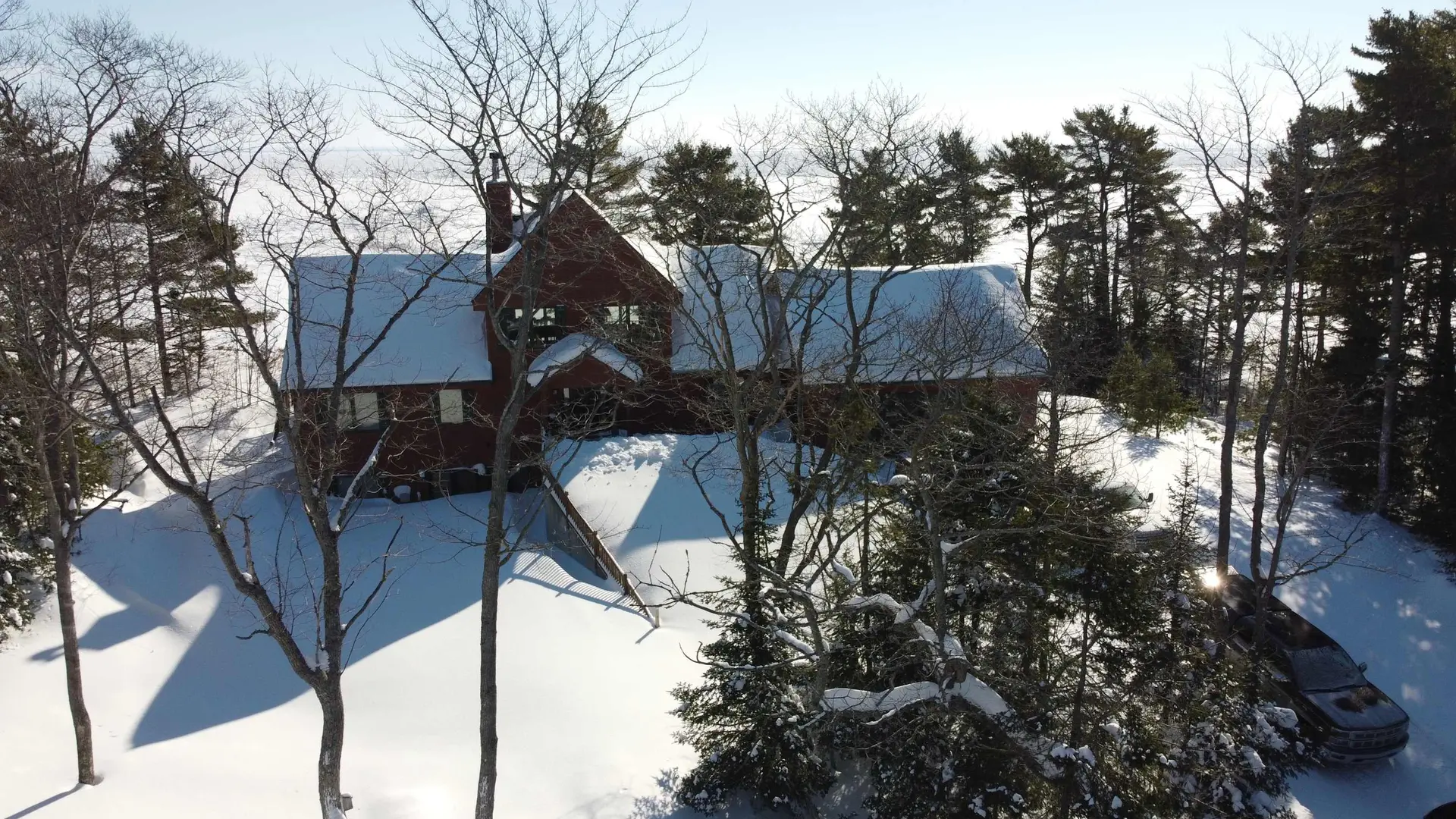 A snow-covered house is surrounded by trees, with a truck visible in the snow.