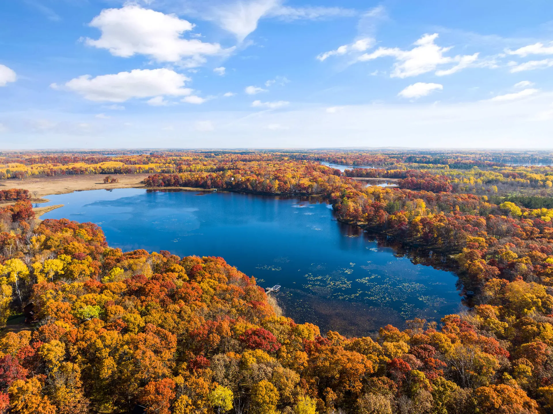 Aerial view of a deep blue lake surrounded by vibrant fall foliage.