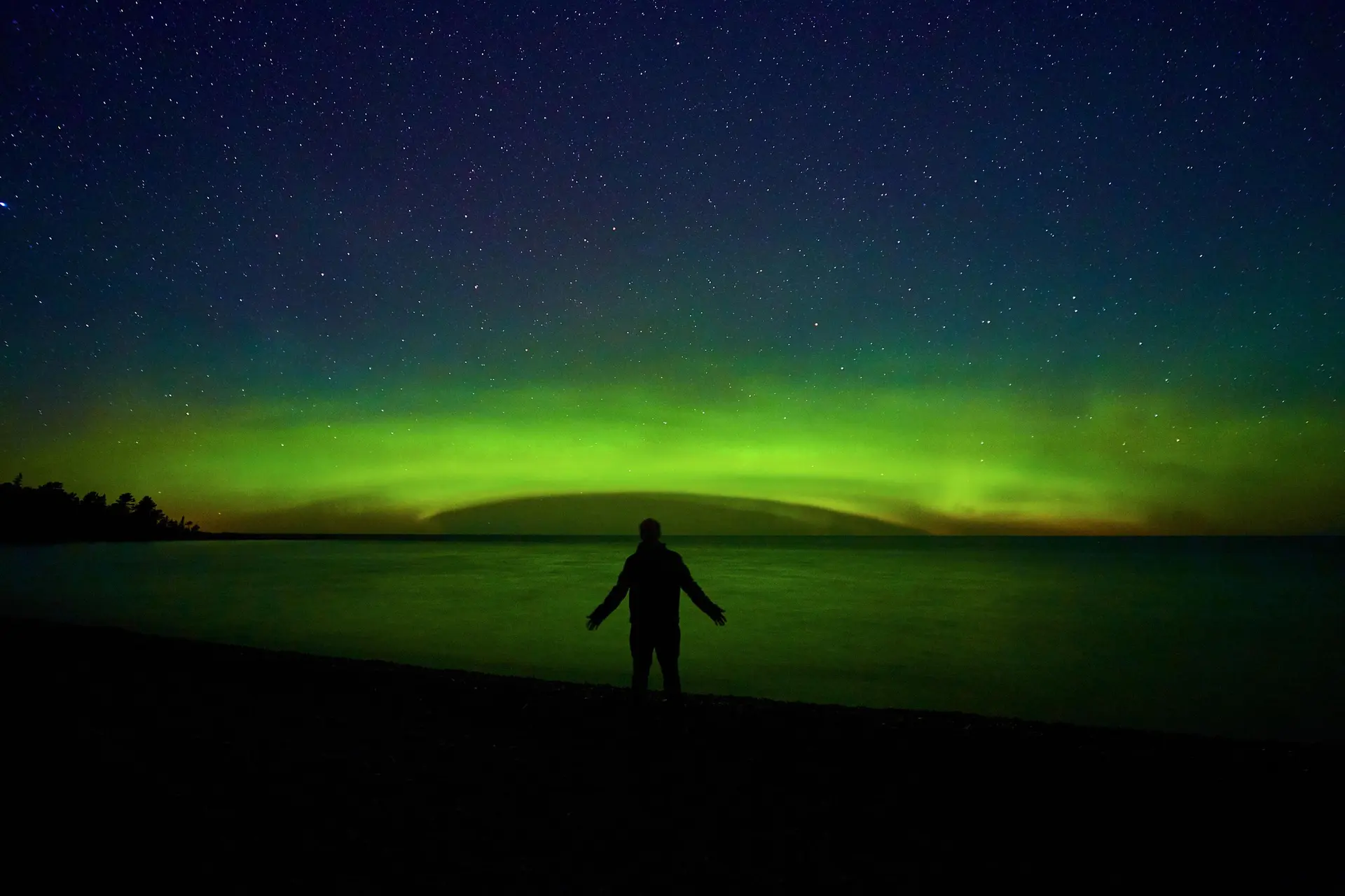 A person watches the aurora borealis over a body of water at night.