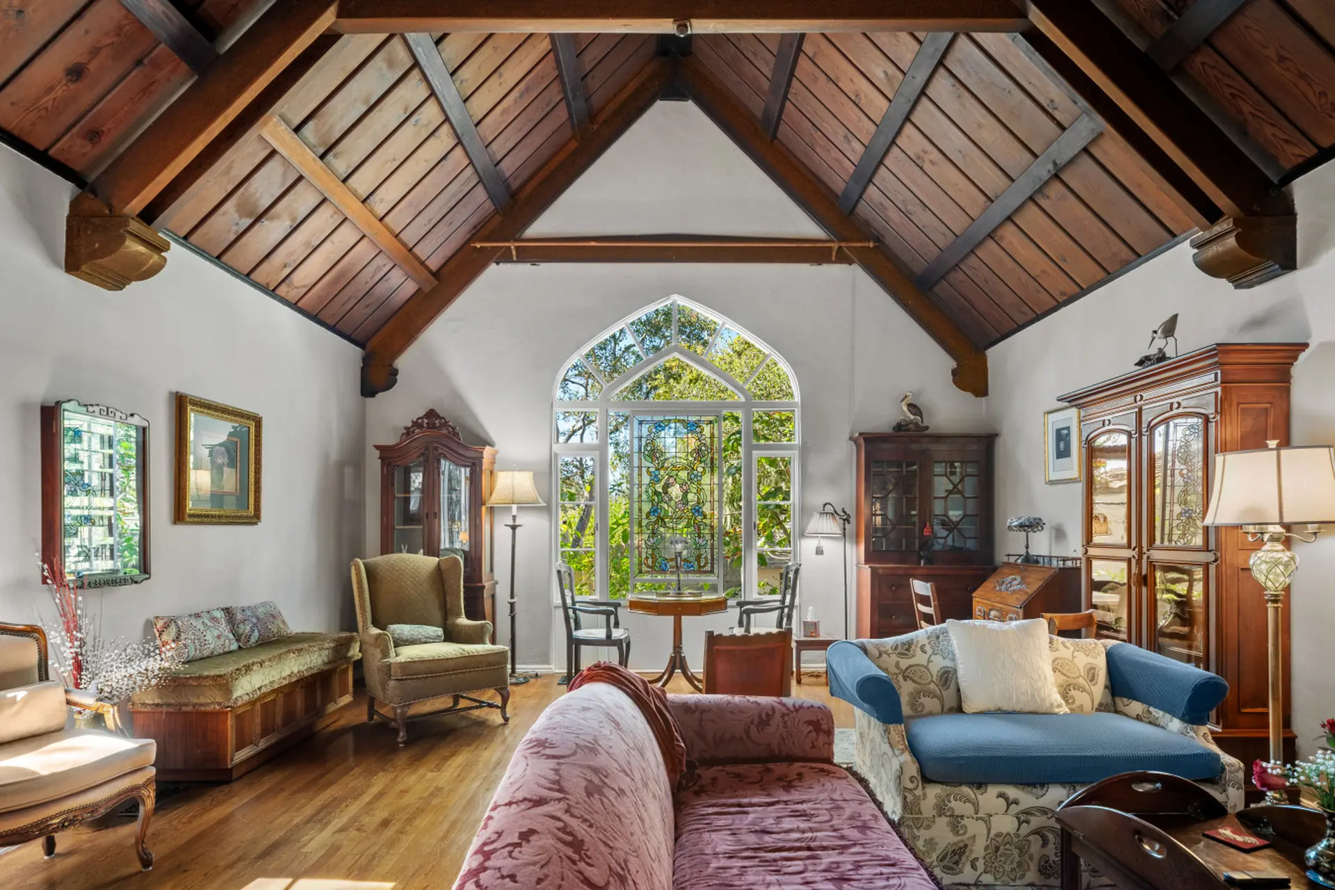 A living room with a vaulted, wooden ceiling and large arched stained-glass window.
