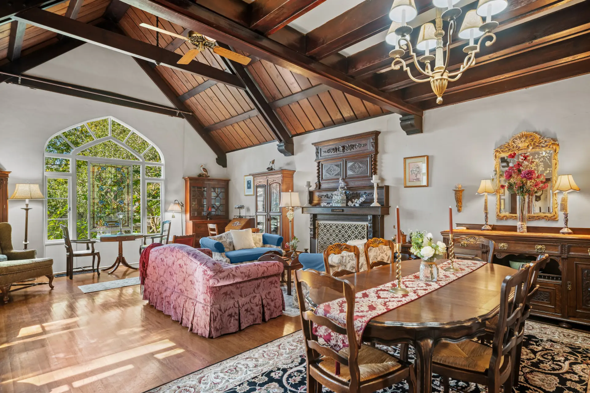 A grand dining room with a wood-beamed ceiling, stained glass window, and antique furniture.