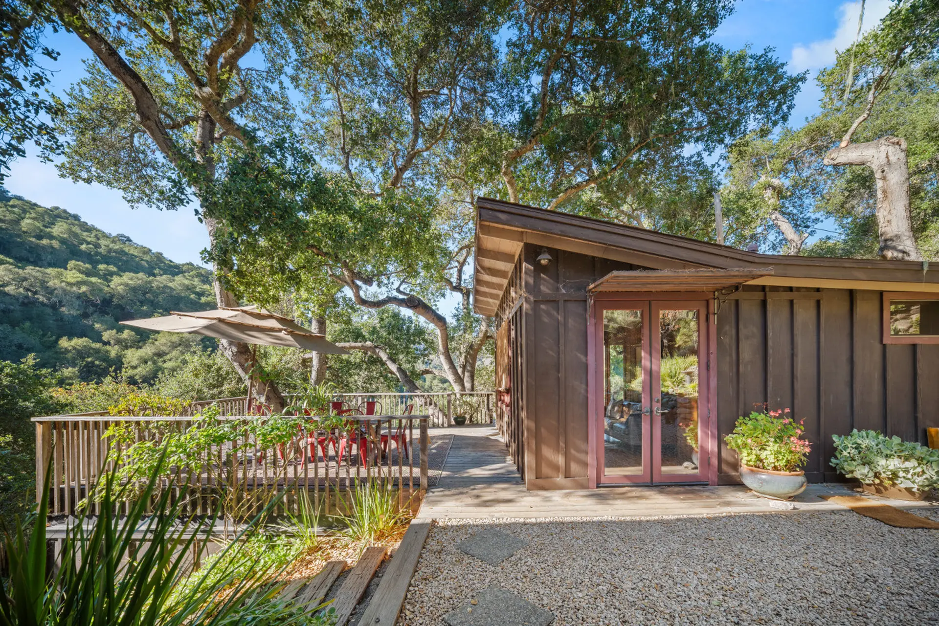 A rustic brown cabin with a wooden deck surrounded by trees.