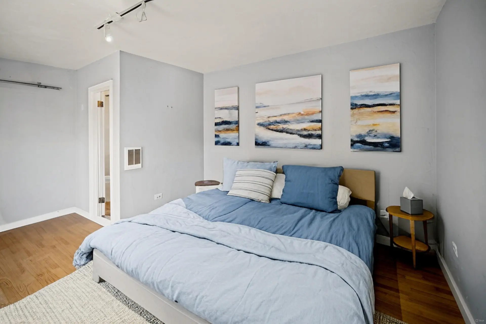 A bedroom with a bed, three abstract paintings, and a small side table.