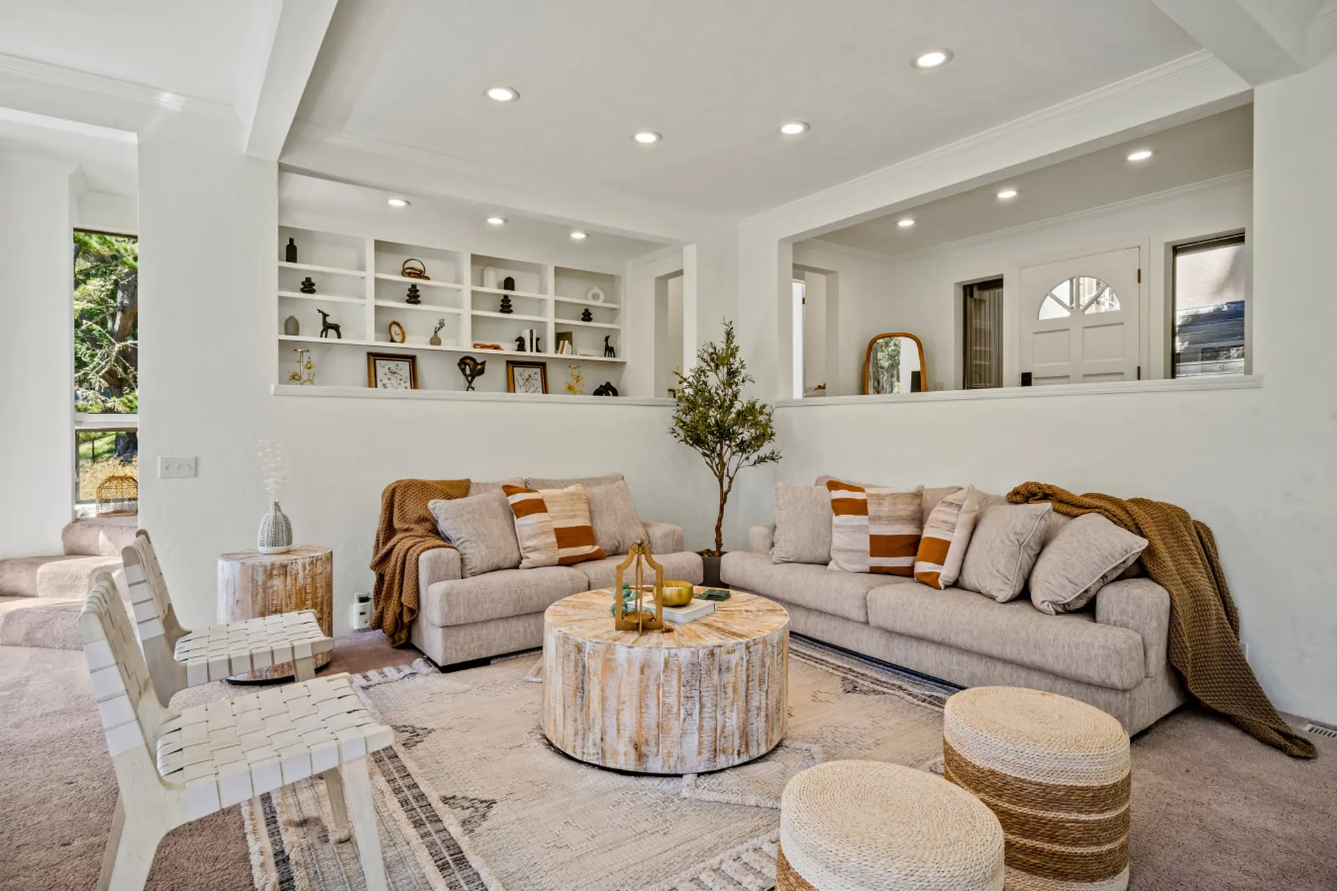 A cozy living room with neutral sofas, patterned pillows, a wood coffee table, and built-in shelving