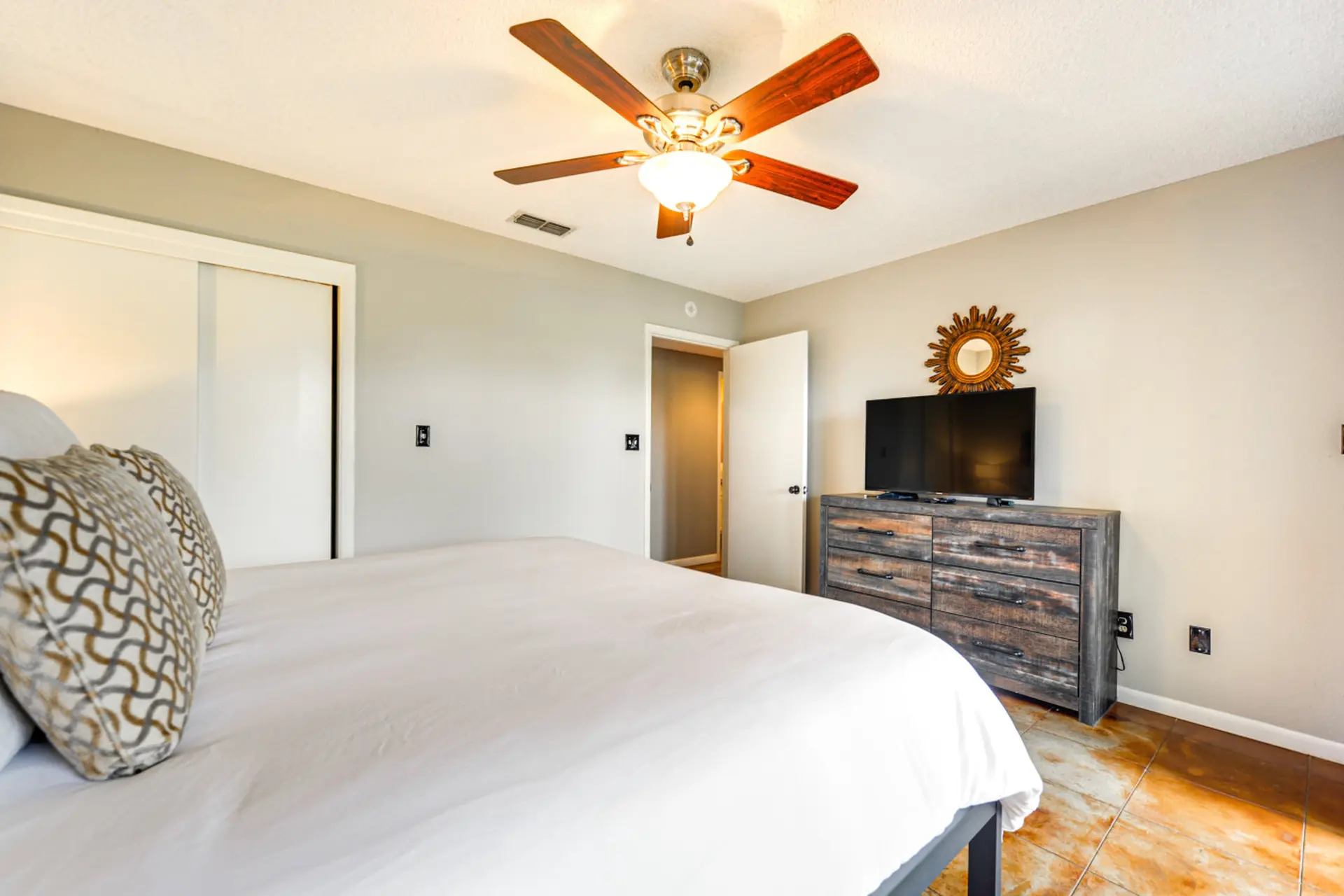 A bedroom with a bed, TV on a dresser, and a ceiling fan.