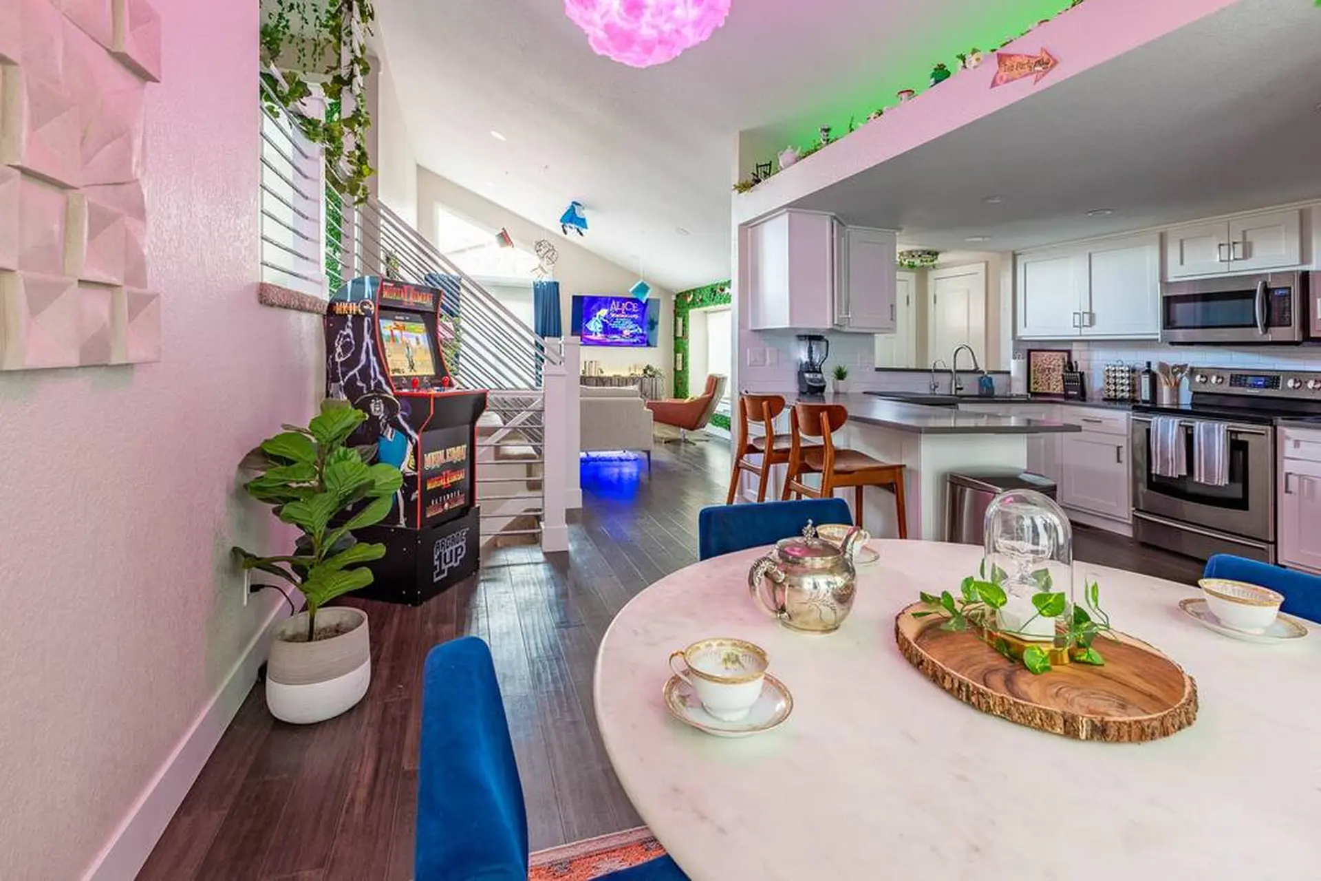 A colorful and modern living and kitchen area with an arcade machine and a dining table.