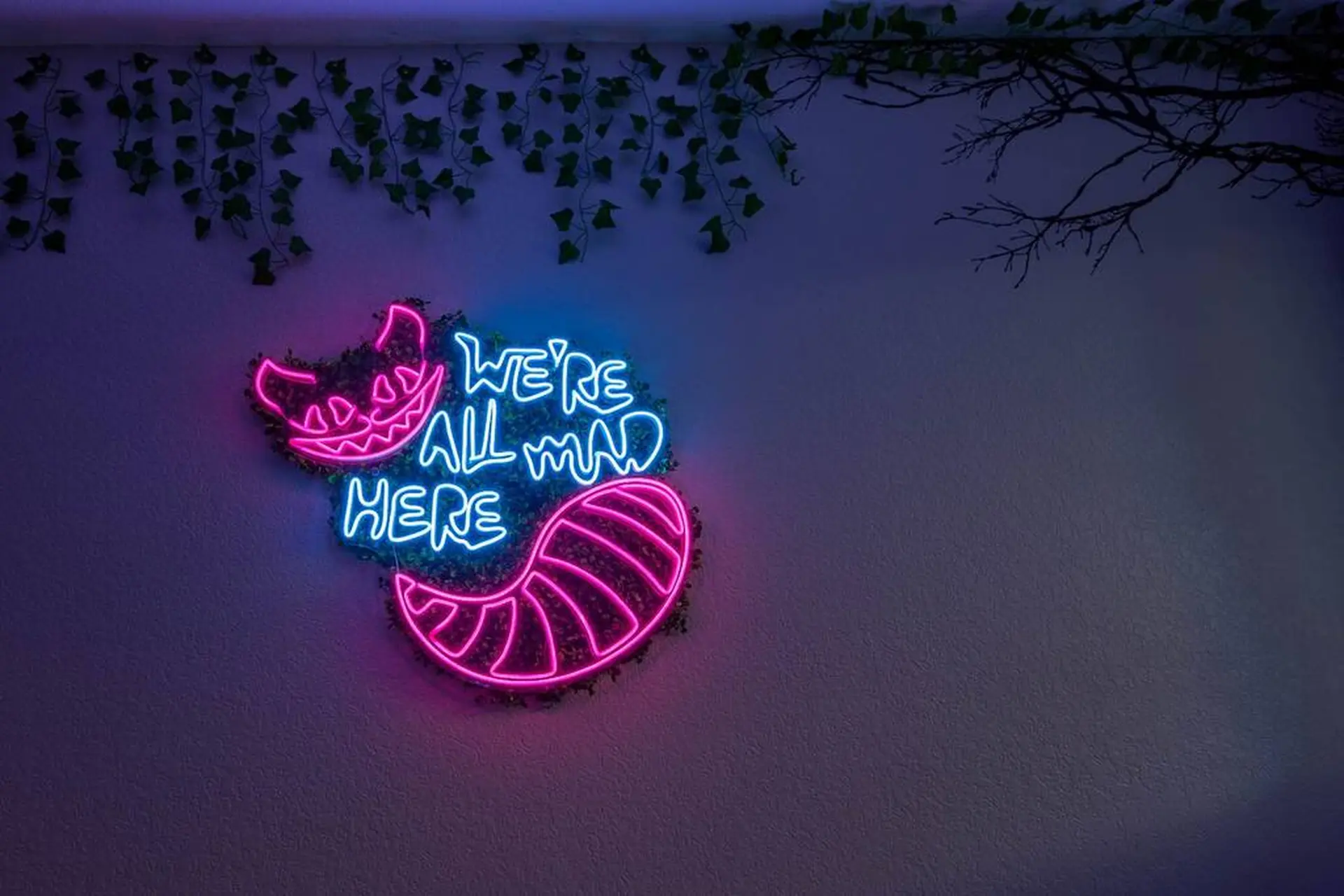 A Cheshire Cat-themed neon sign that says "We're All Mad Here" hangs on a wall.