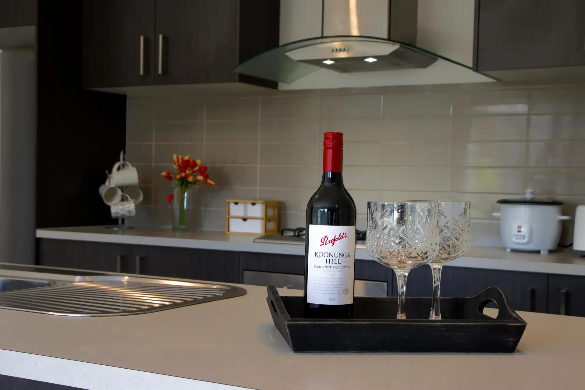 A bottle of Penfolds Koonunga Hill Cabernet Sauvignon rests in a black wooden tray with two crystal 