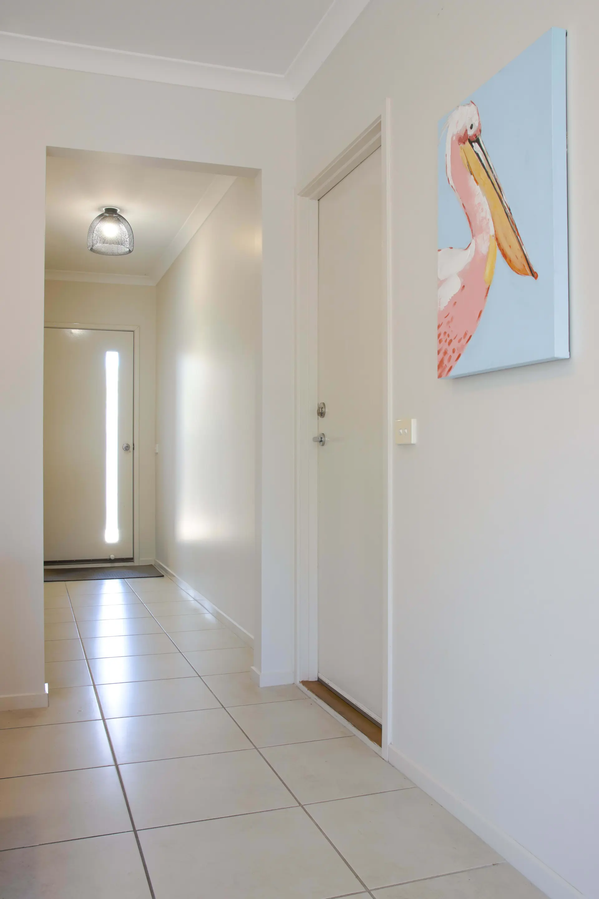 An abstract painting of a pelican hangs on a hallway wall next to a door.