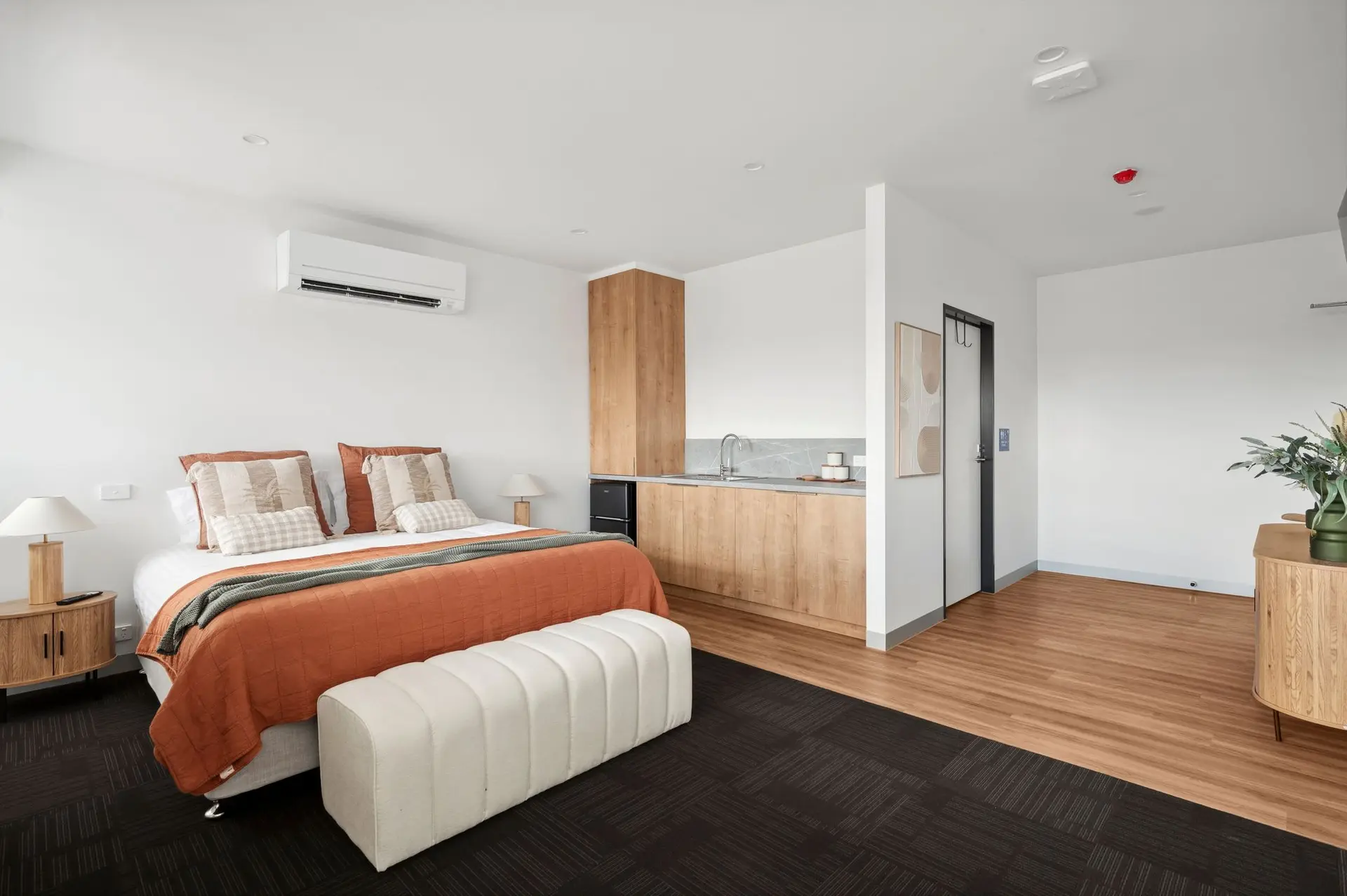 Bedroom with a bed, kitchenette, and a bench.