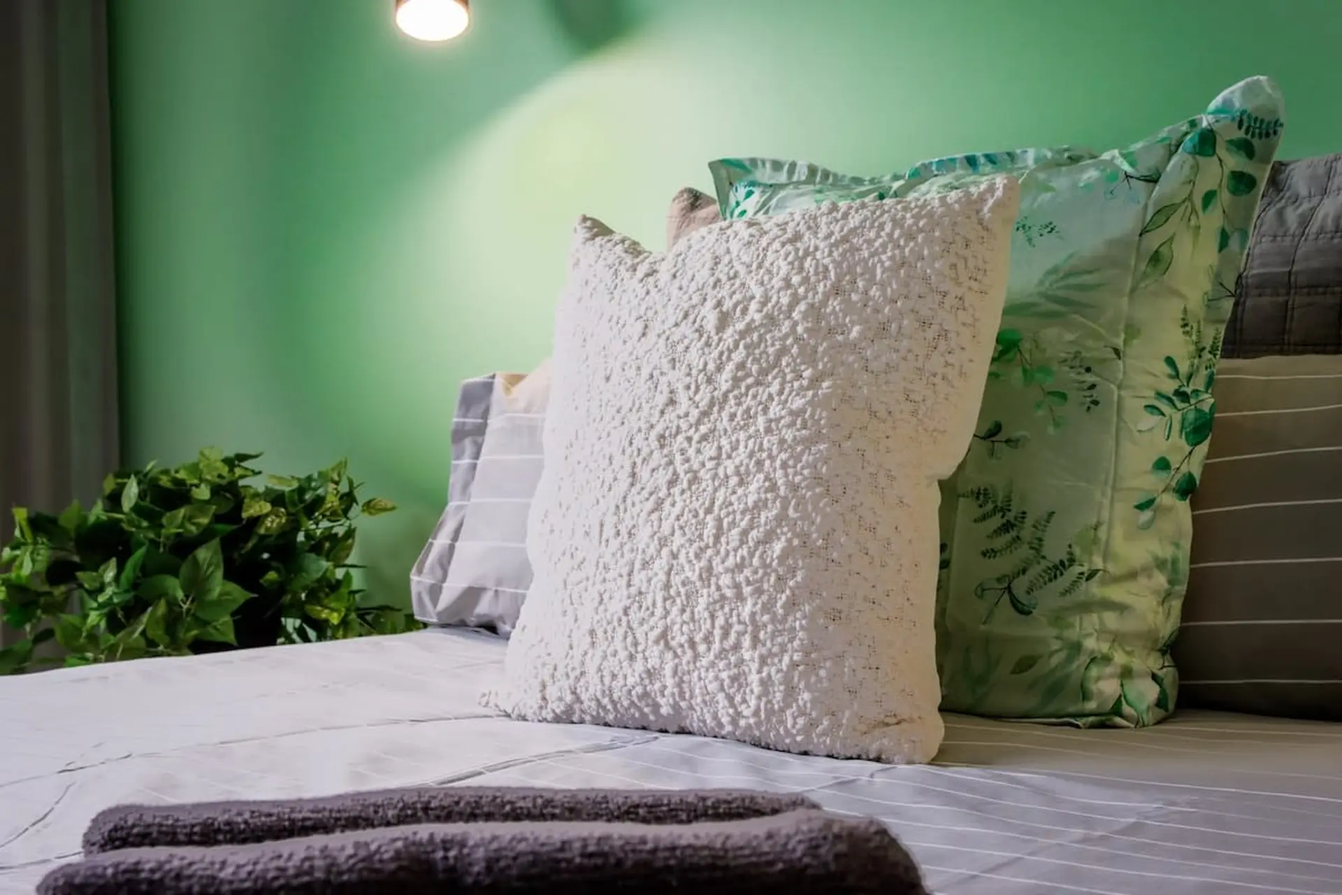 A close-up of a bed with textured white and green botanical print pillows.