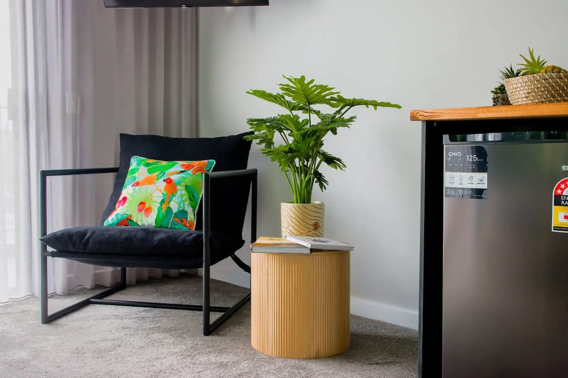 A black armchair with a tropical pillow sits next to a side table with a plant.