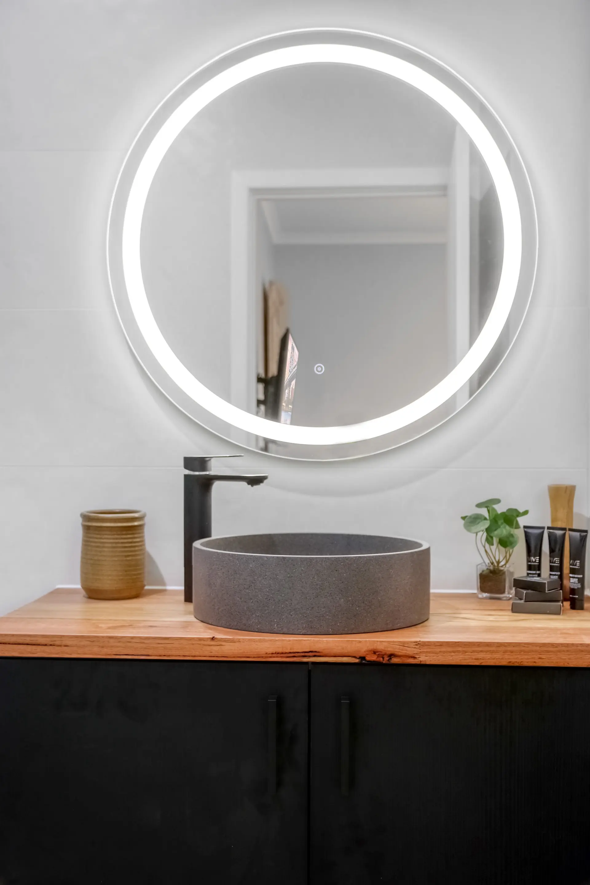 A minimalist bathroom vanity with a stone sink, a modern faucet, and a lighted mirror.