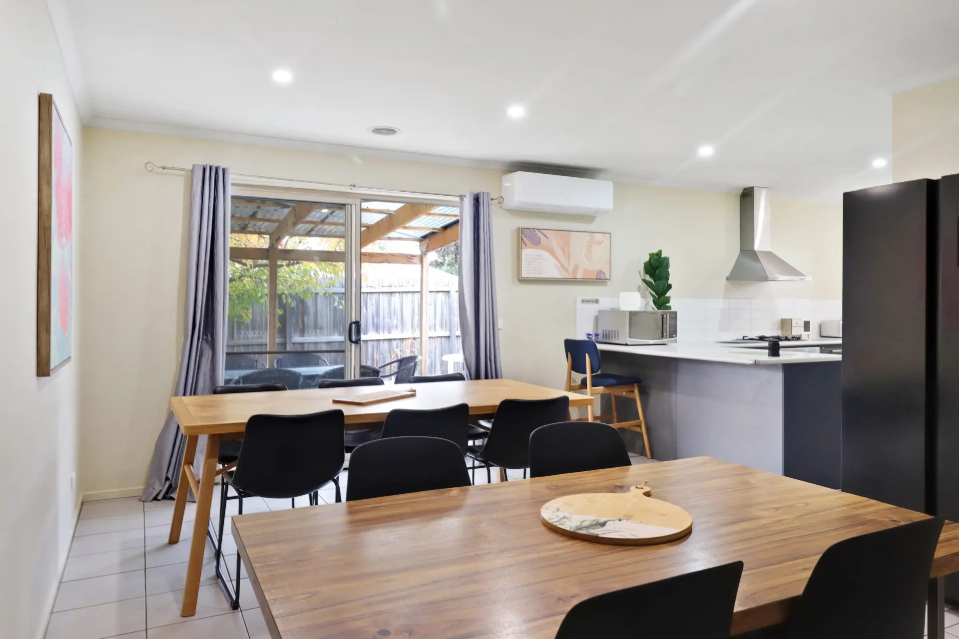 A modern dining area with two tables, black chairs, and a kitchen counter.