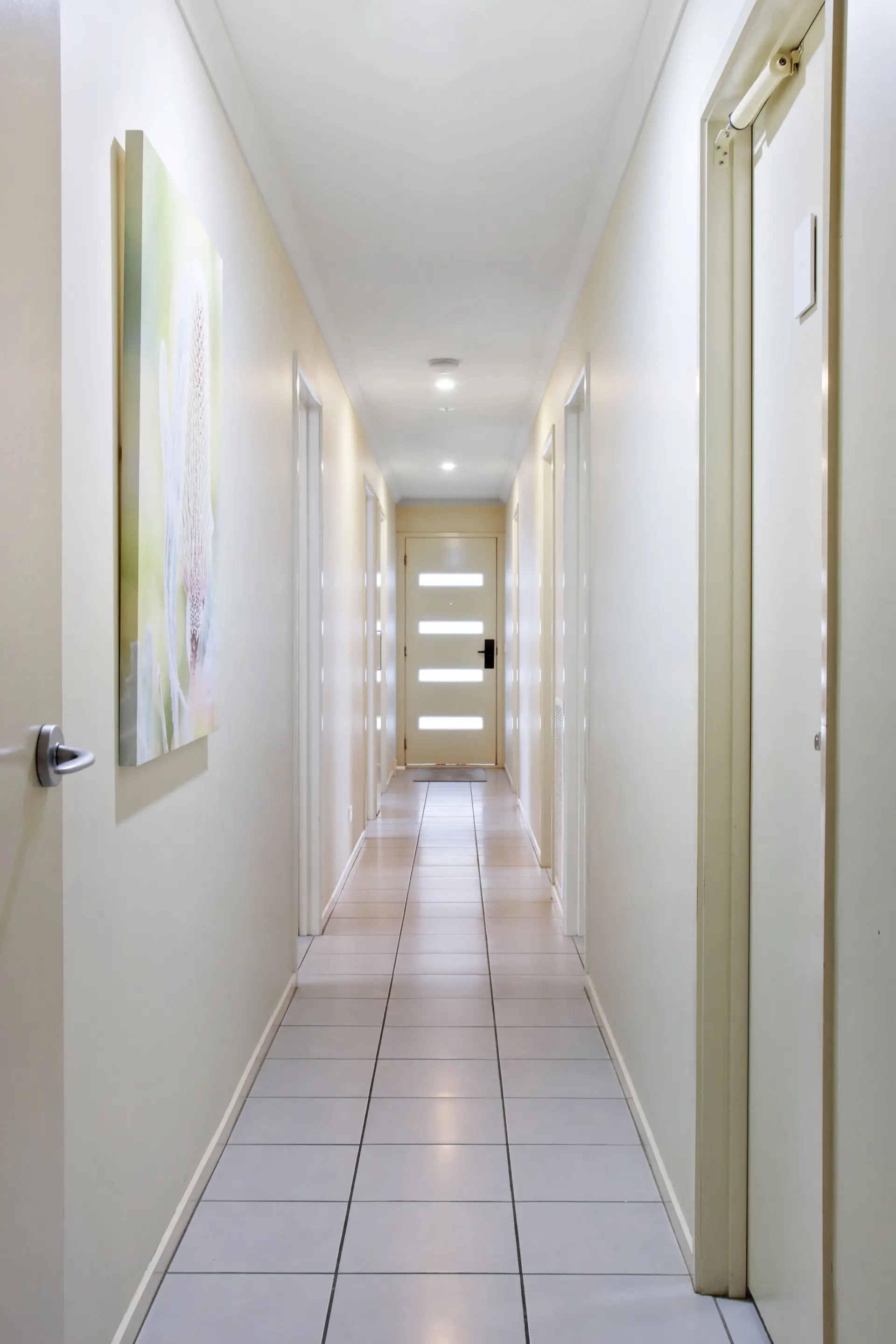A long hallway with white doors and a painting on the wall.
