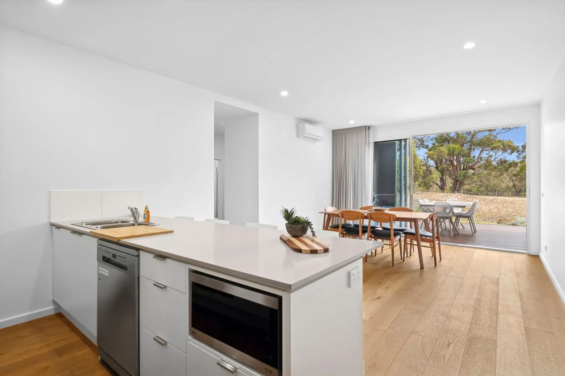 A modern kitchen and dining area with sliding glass doors opening to a natural landscape.