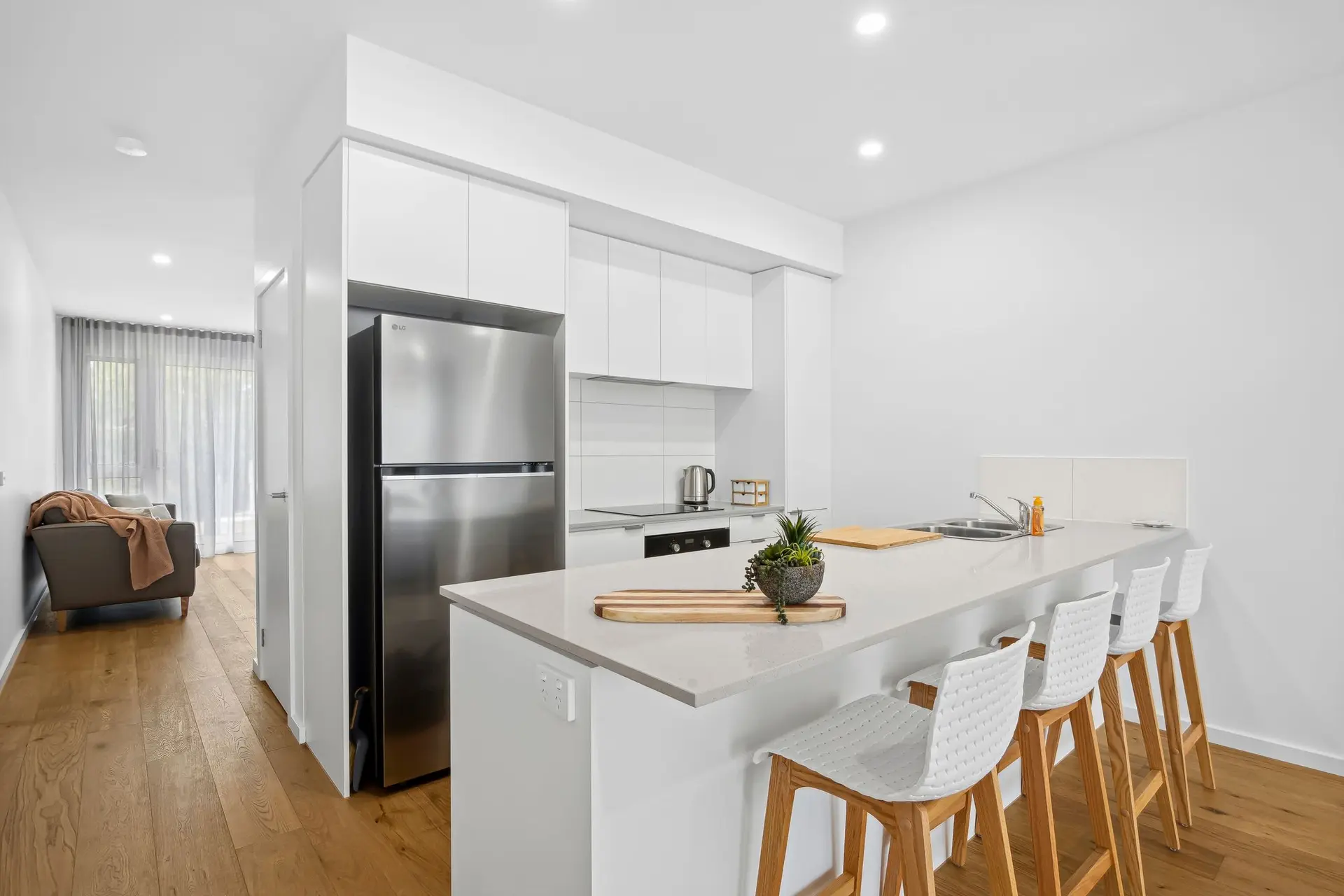 A modern kitchen with white cabinets, stainless steel appliances, and a breakfast bar with four stoo