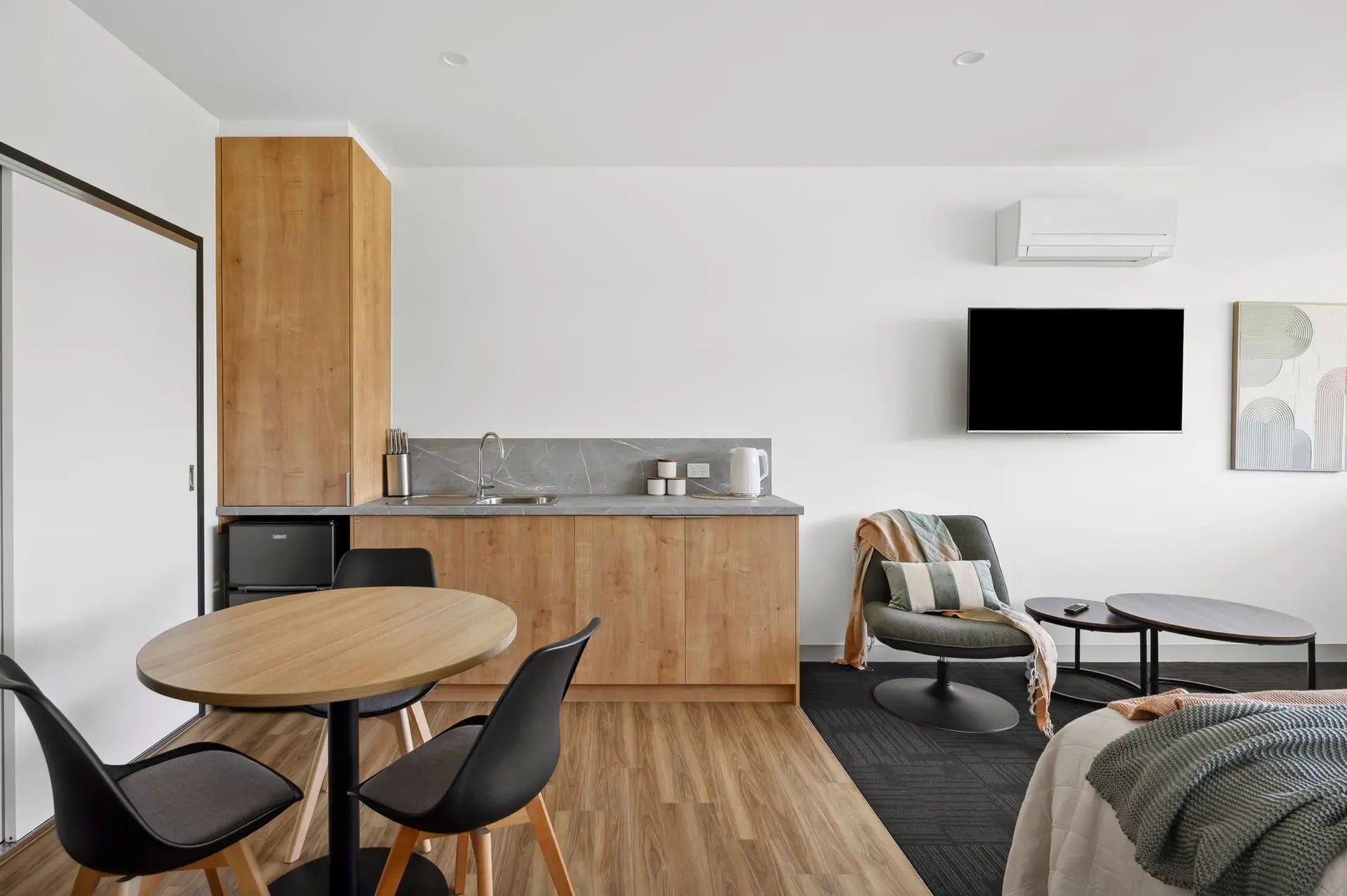 A modern studio apartment with a kitchenette, dining table, and living area with a tv and armchair.