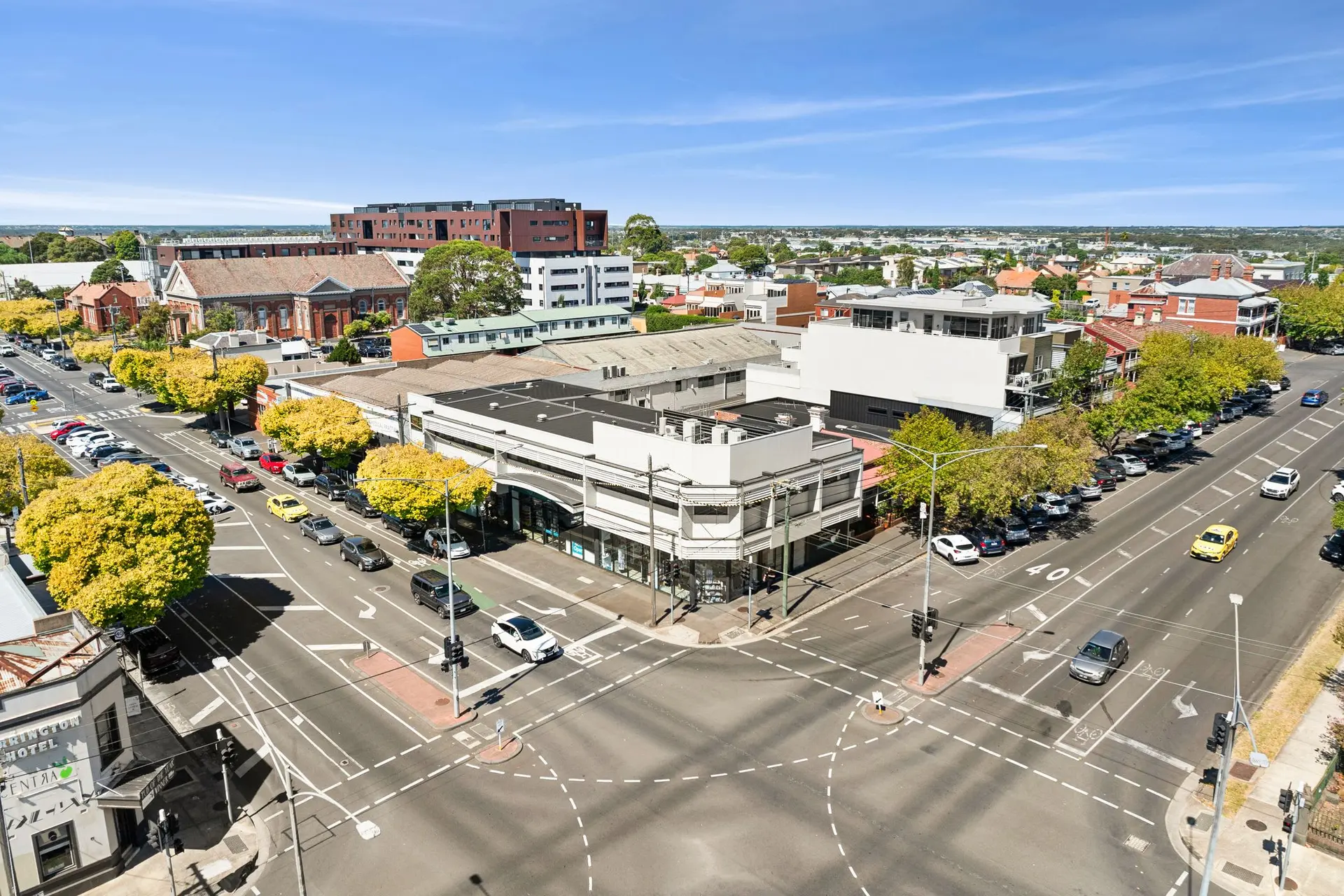 An aerial view of a sunny intersection with buildings, trees, and cars.