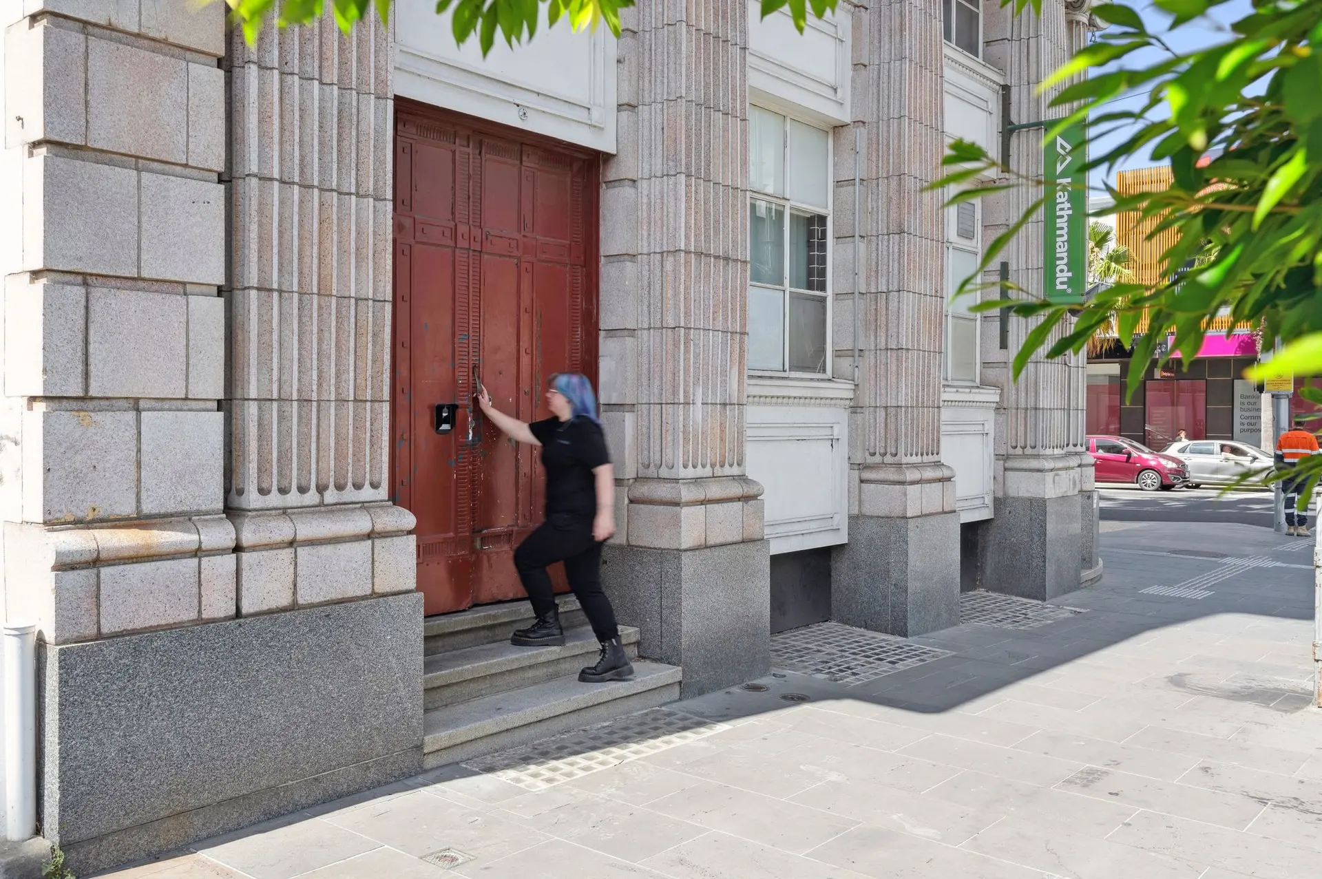 A person with blue hair walks up stairs toward a red door.