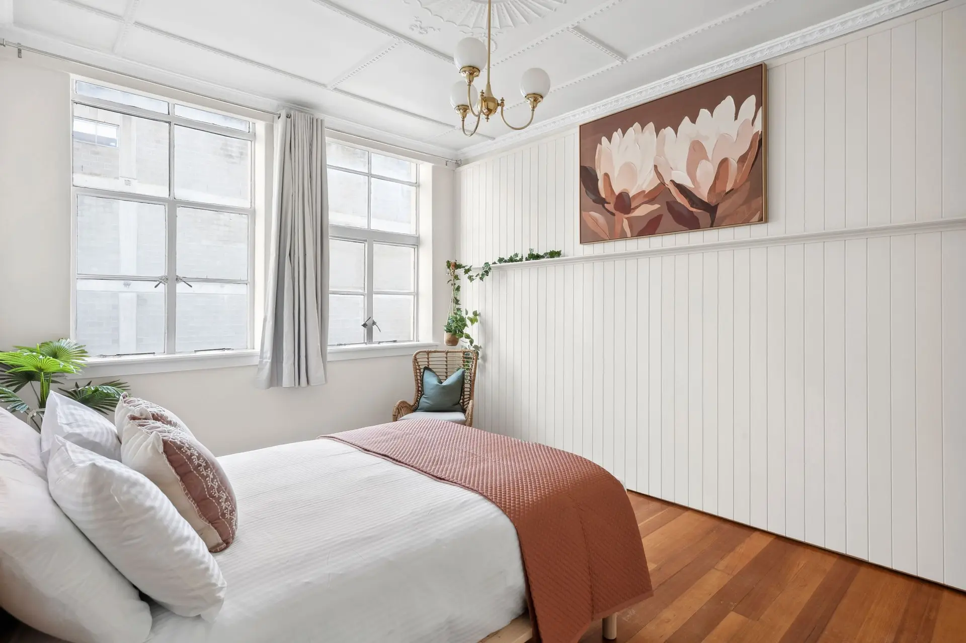 A modern bedroom with a bed, a wicker chair, and artwork on a paneled wall.