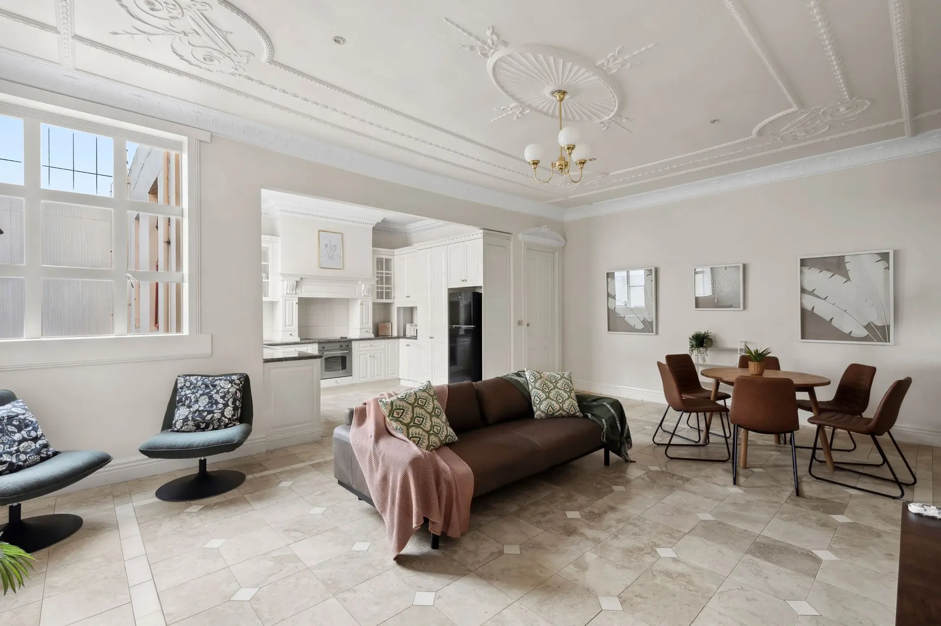A luxurious living and dining room with a brown leather sofa, dining set, and patterned pillows.