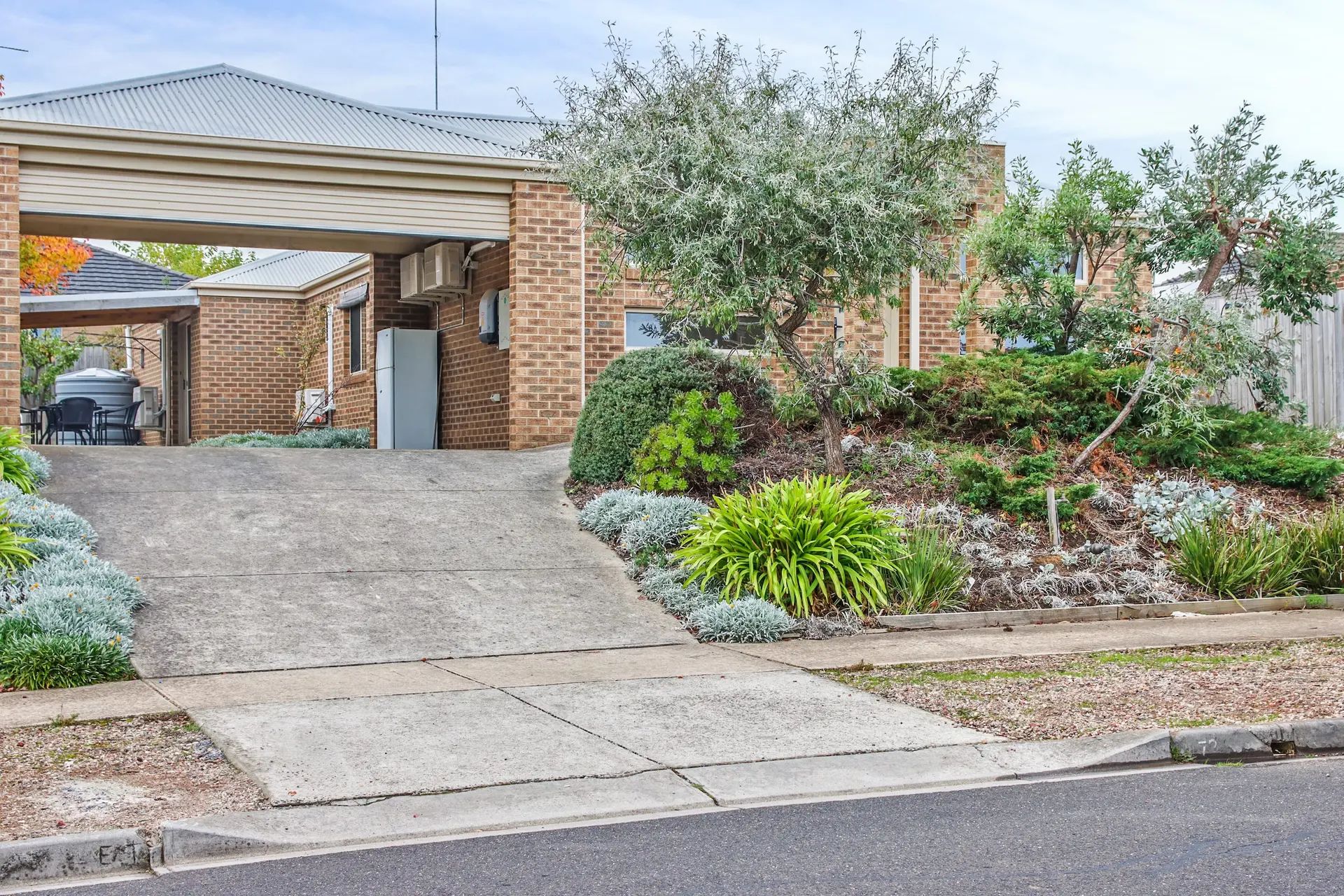 A paved driveway leads to a brick house with a carport and a well-landscaped garden.